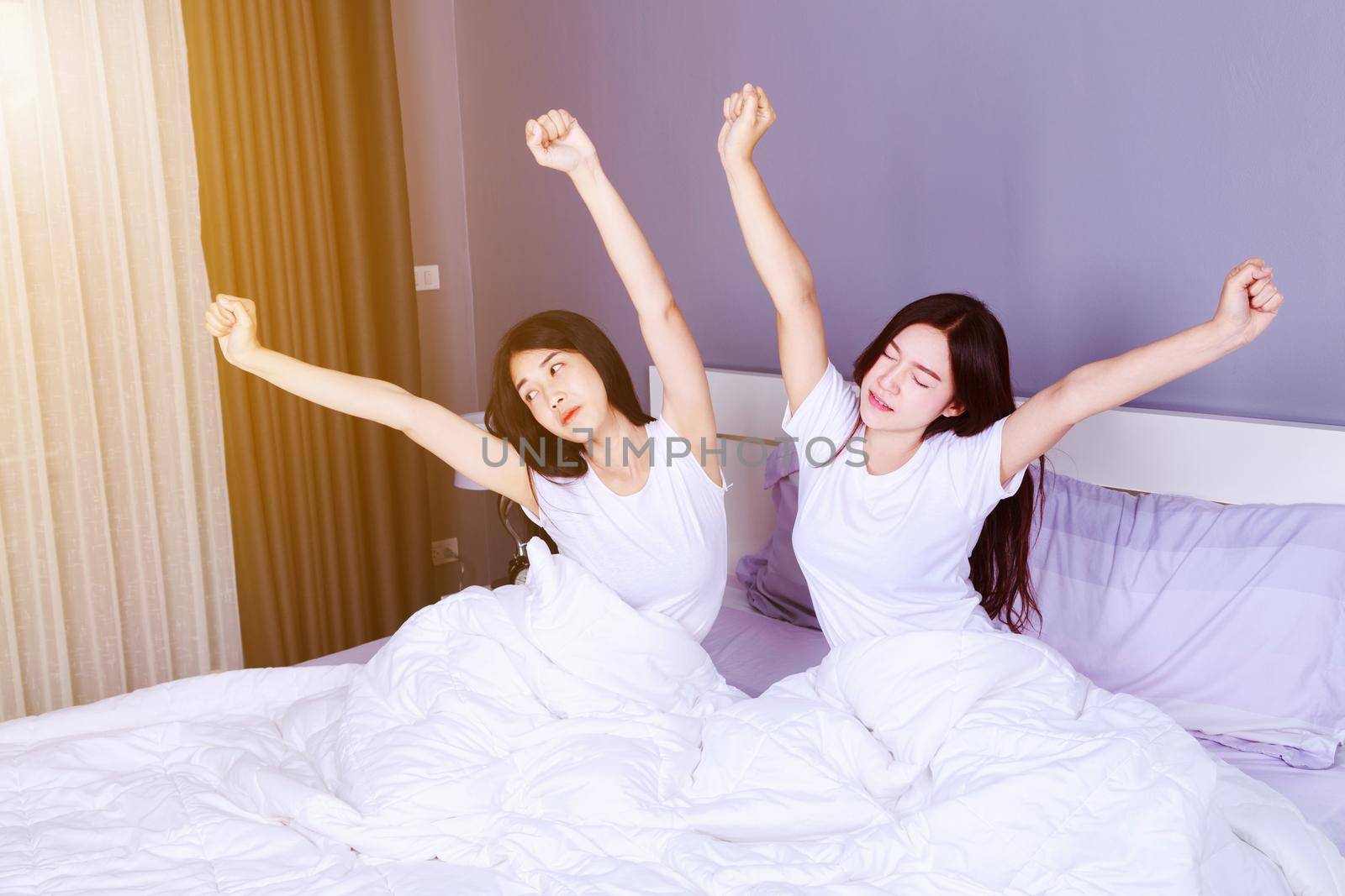 two woman waking up and hand raised on bed in the bedroom