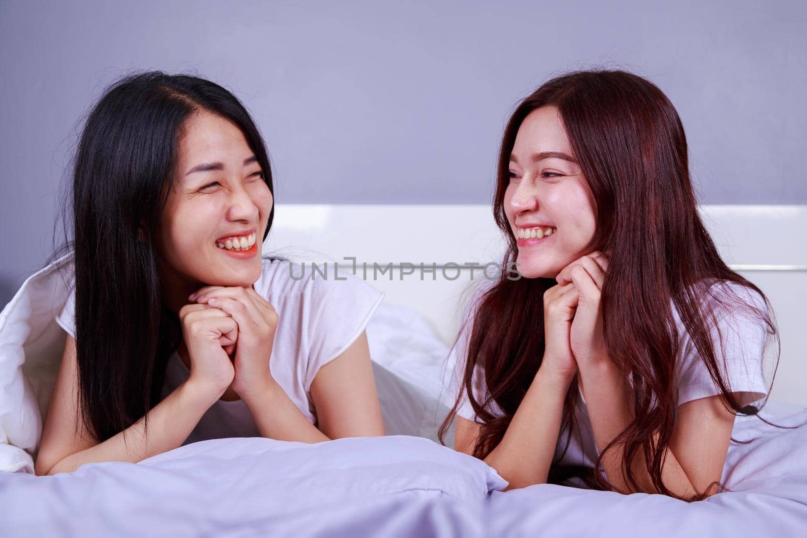 two happy woman lying on bed in bedroom by geargodz