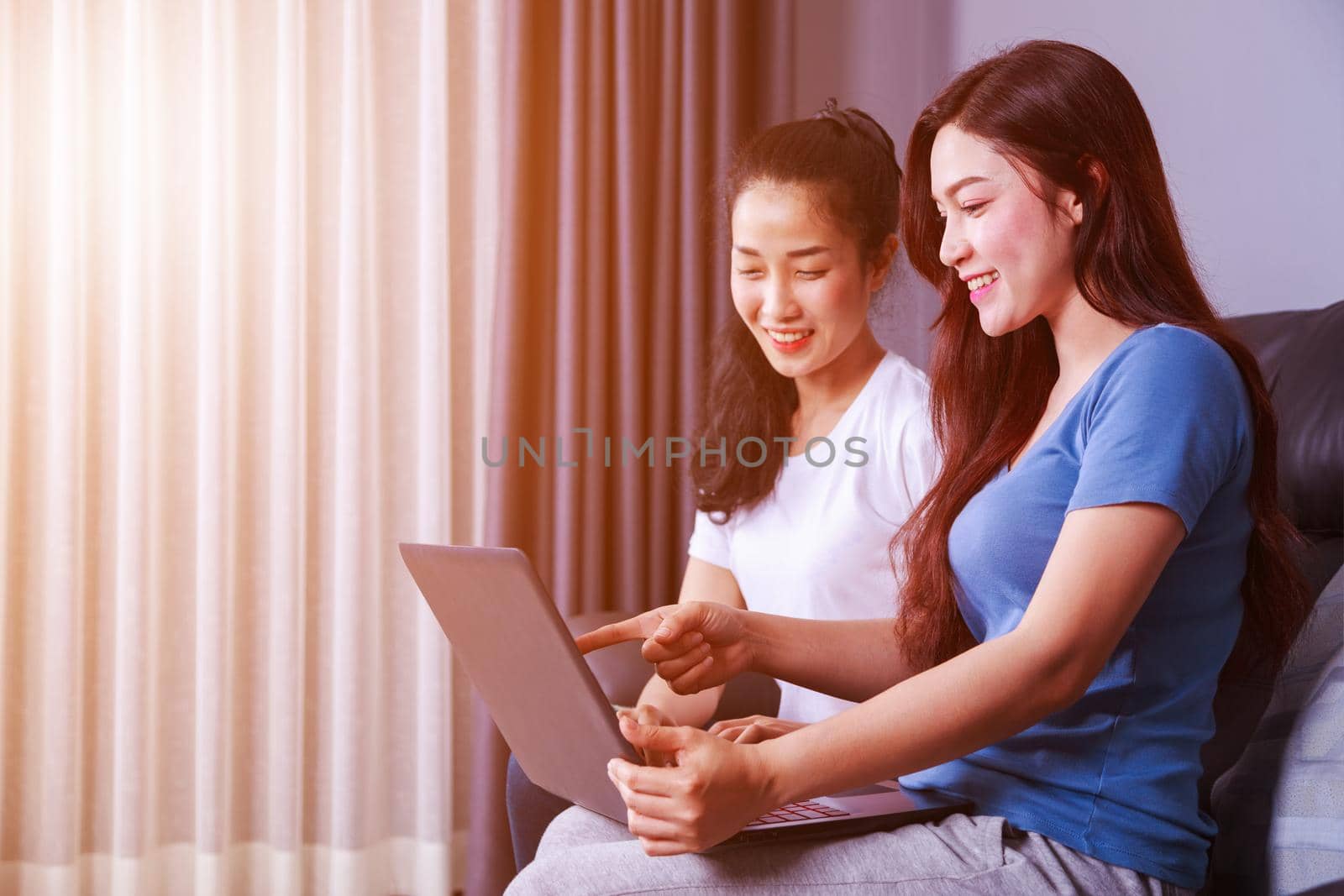 two young woman using a laptop computer on sofa in living room at home
