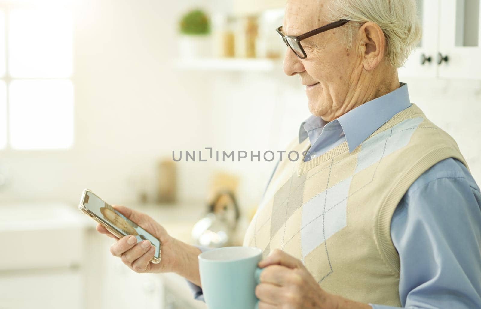 Friendly elderly gentleman weating glasses while looking at smartphone screen during a video call with medical doctor