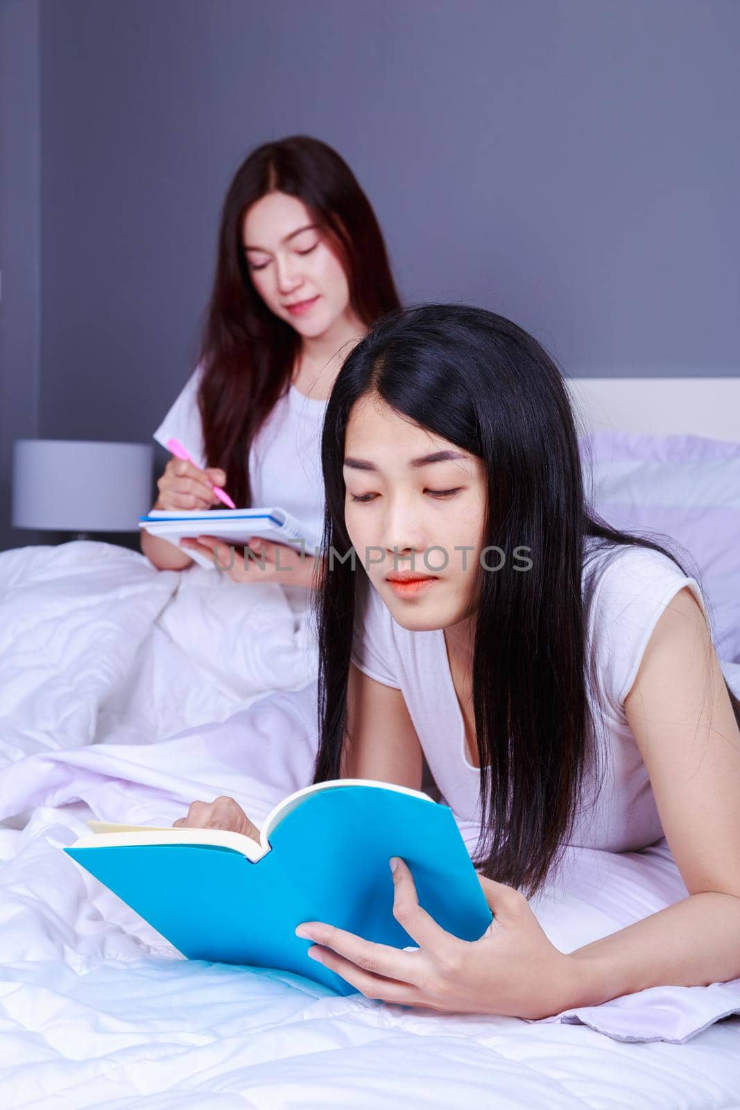 two woman writing and reading a book on bed in the bedroom