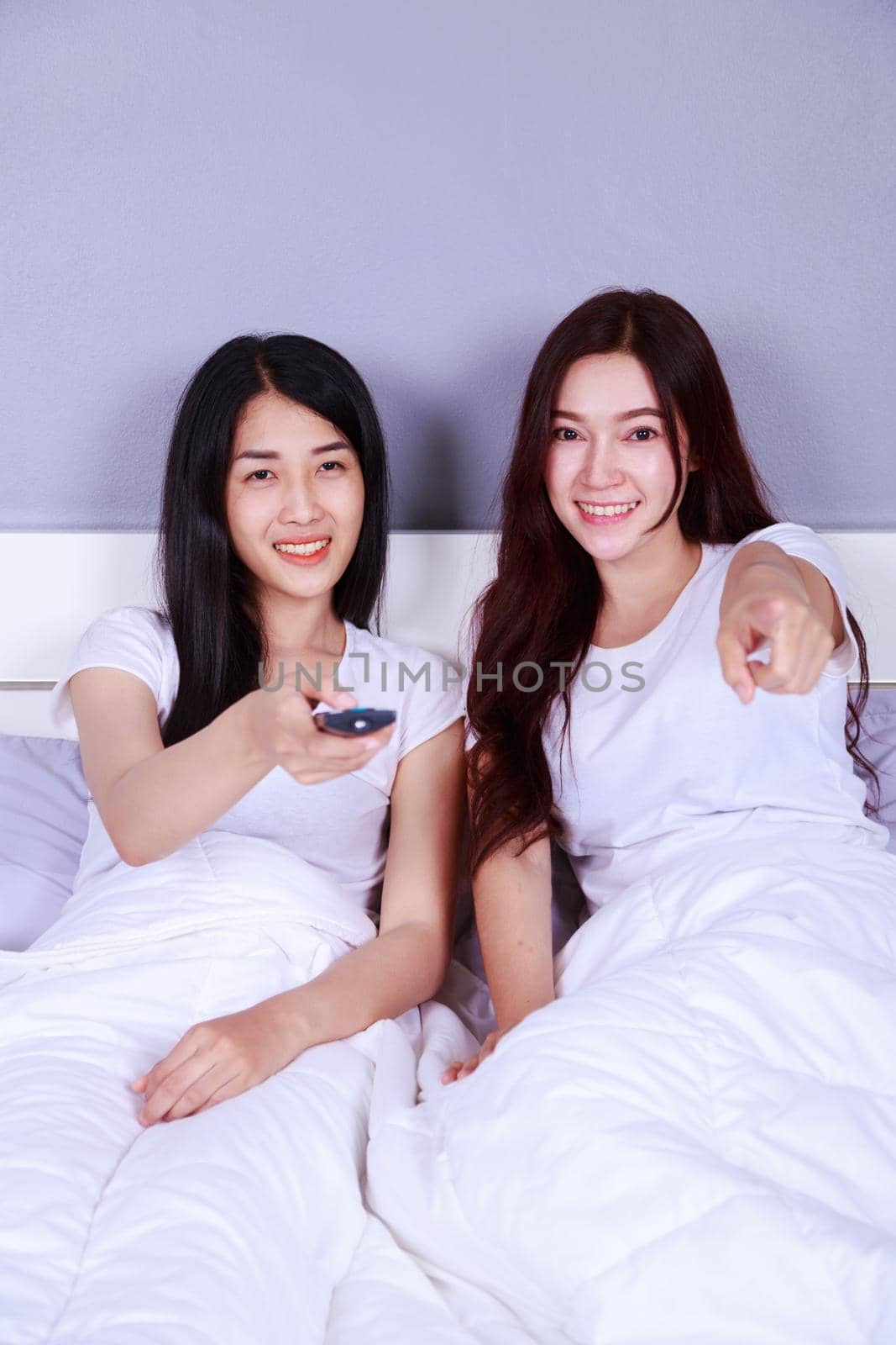 two best friends watching tv with remote on bed in the bedroom