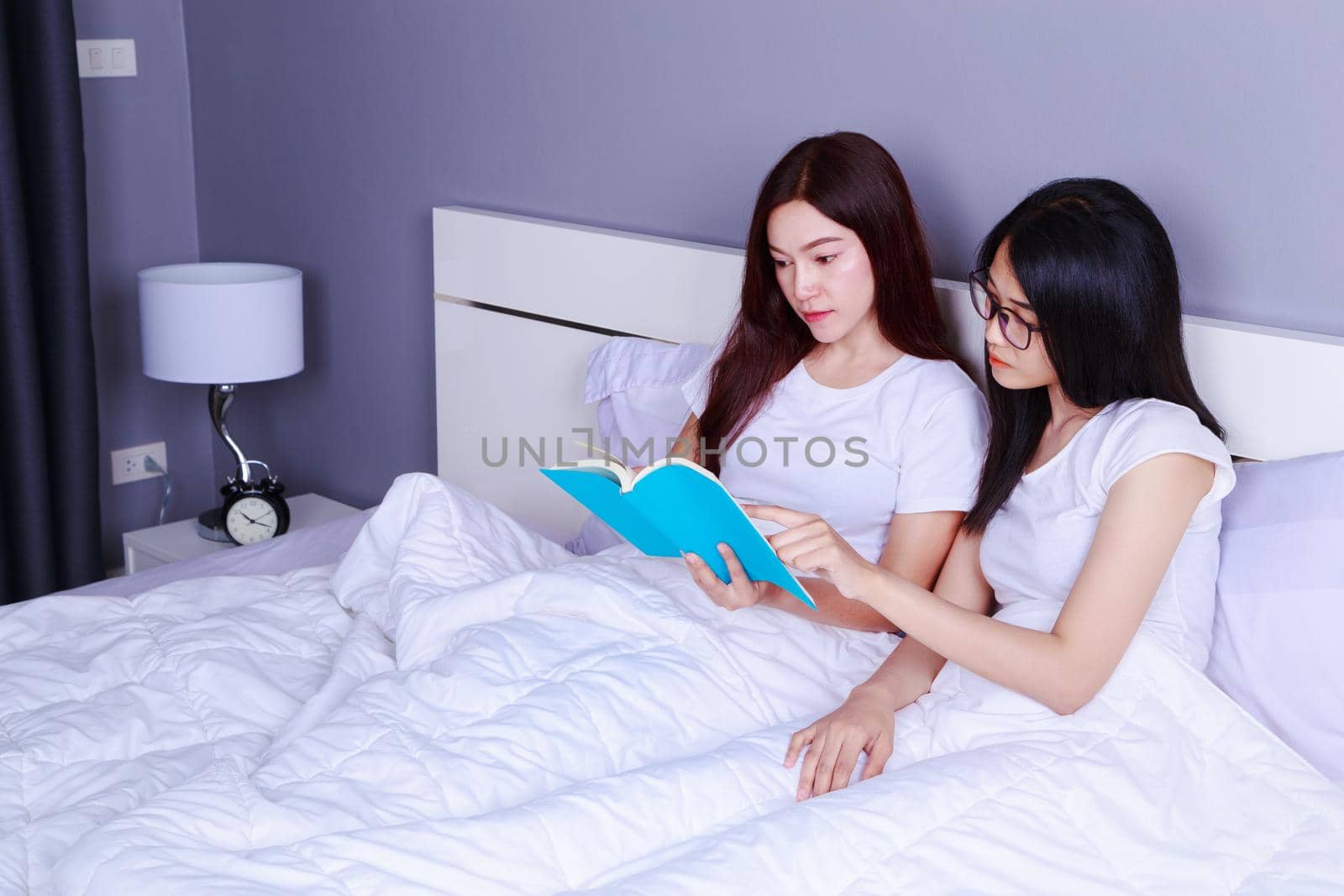 two woman reading a book on bed in bedroom by geargodz