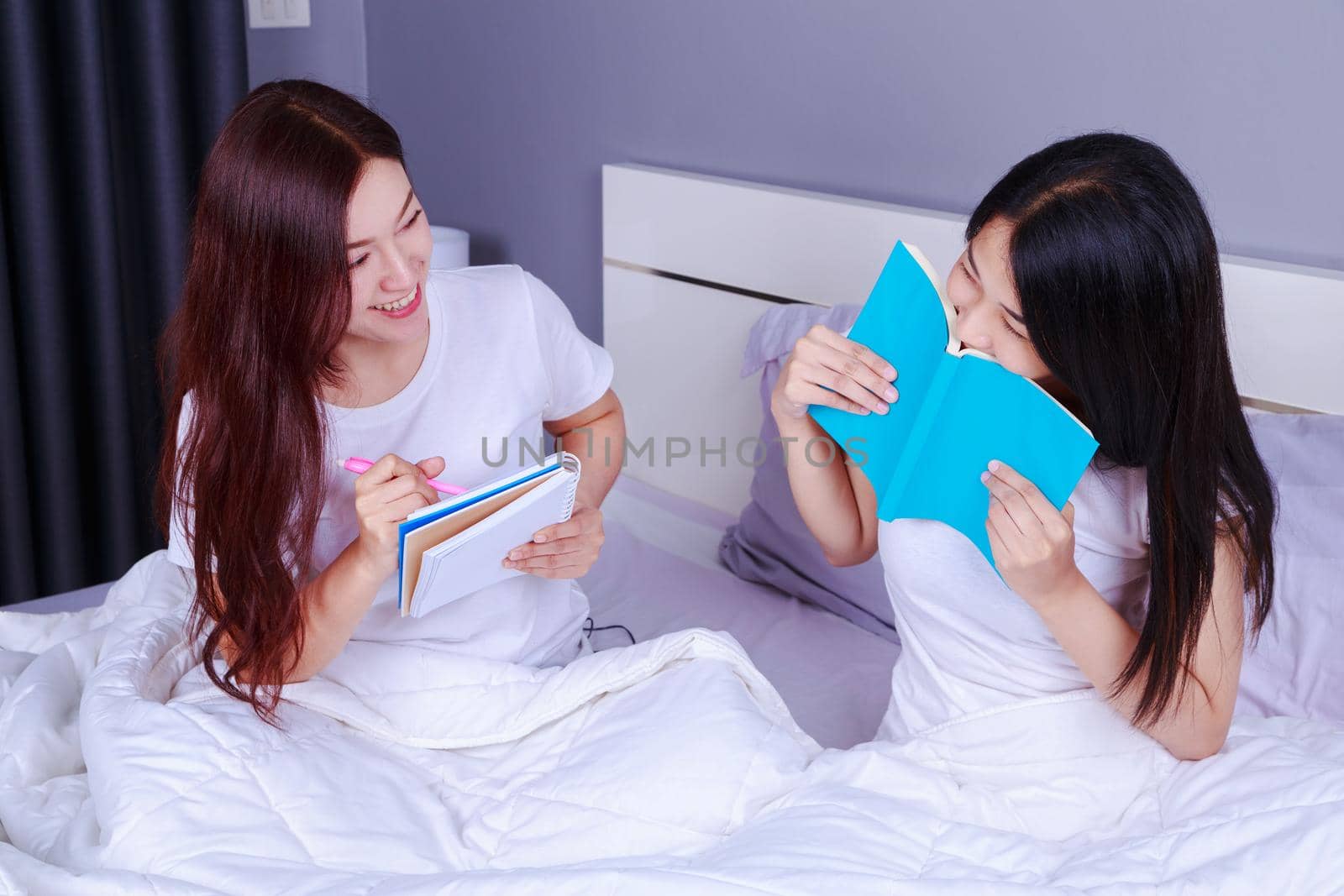 two woman writing and reading a book on bed in the bedroom