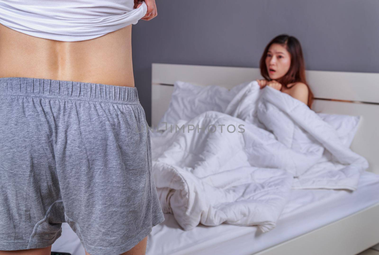 couple in bedroom is having sex, man taking his clothes off with woman sitting on a bed