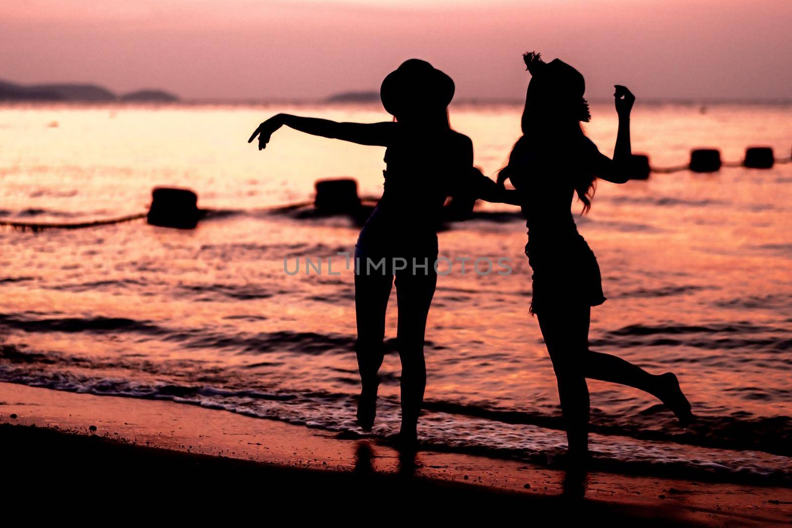 Silhouette of two young woman having fun on the sea beach