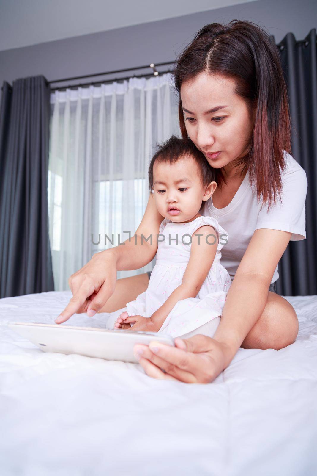 Mother and baby are looking to play and read tablet computer on bed at home