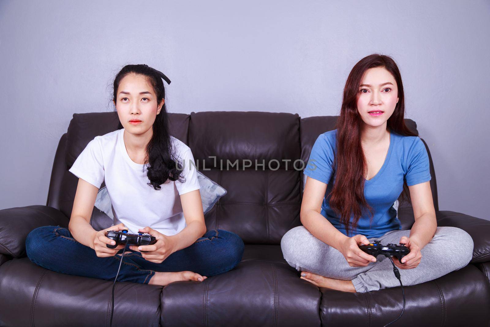 two young woman using joystick controller playing video game on sofa at home by geargodz