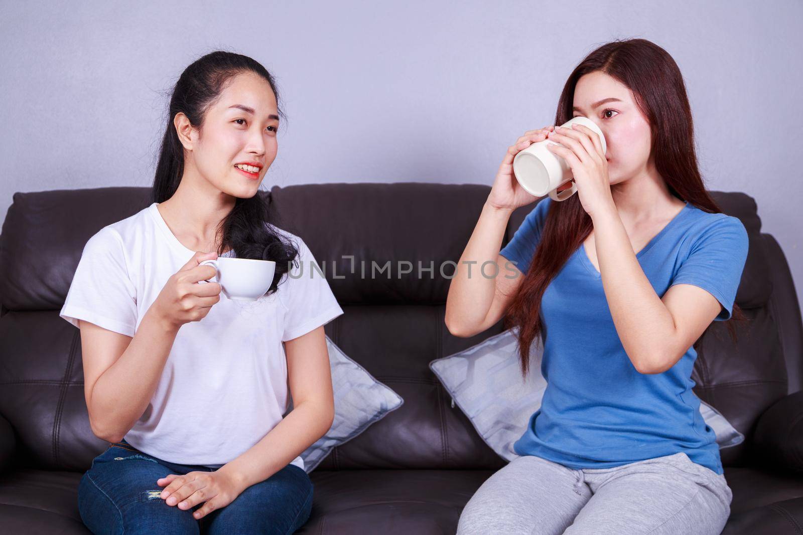two best friends talking and drinking a cup of coffee on sofa in living room by geargodz