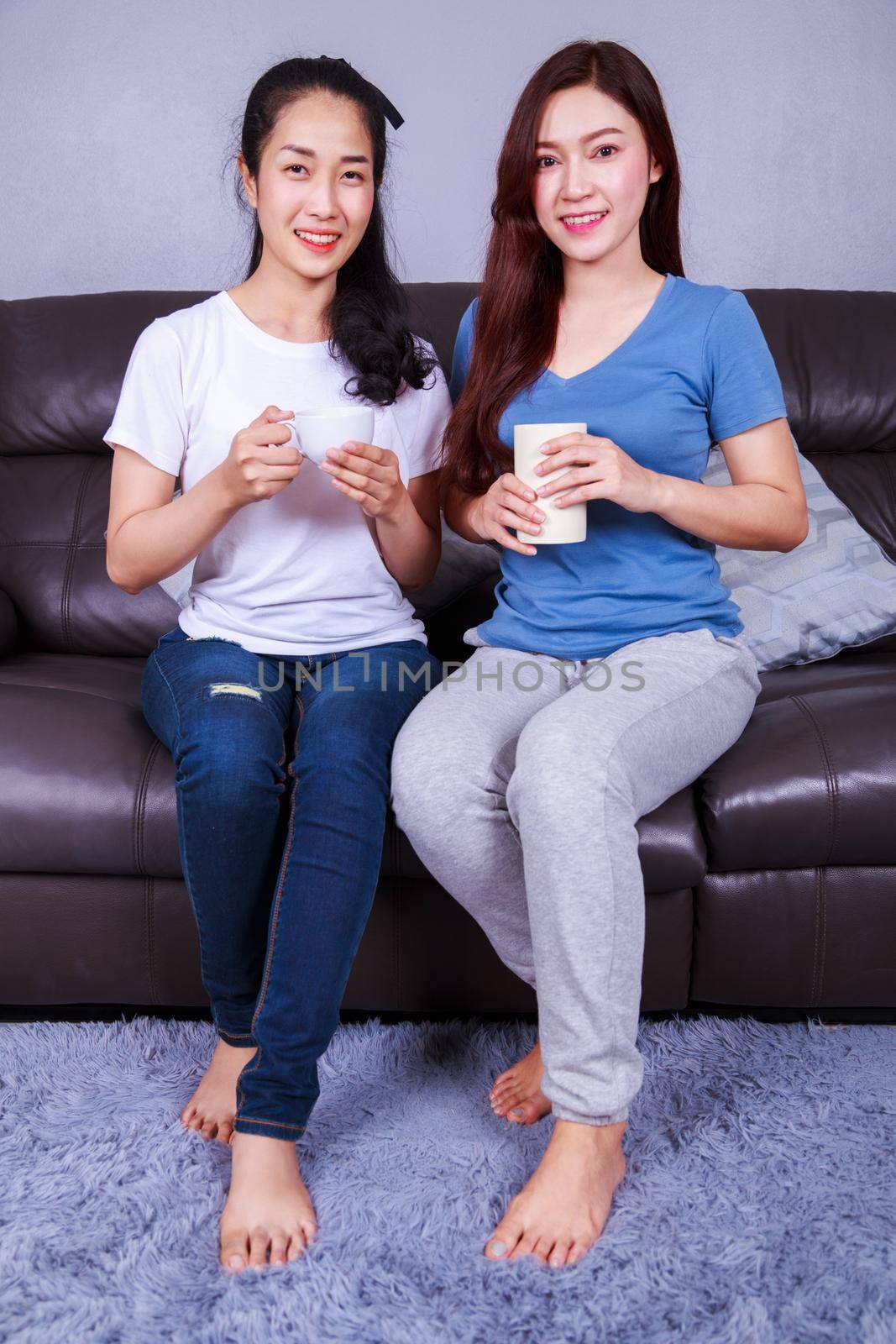 two best friends talking and drinking a cup of coffee on sofa in living room at home