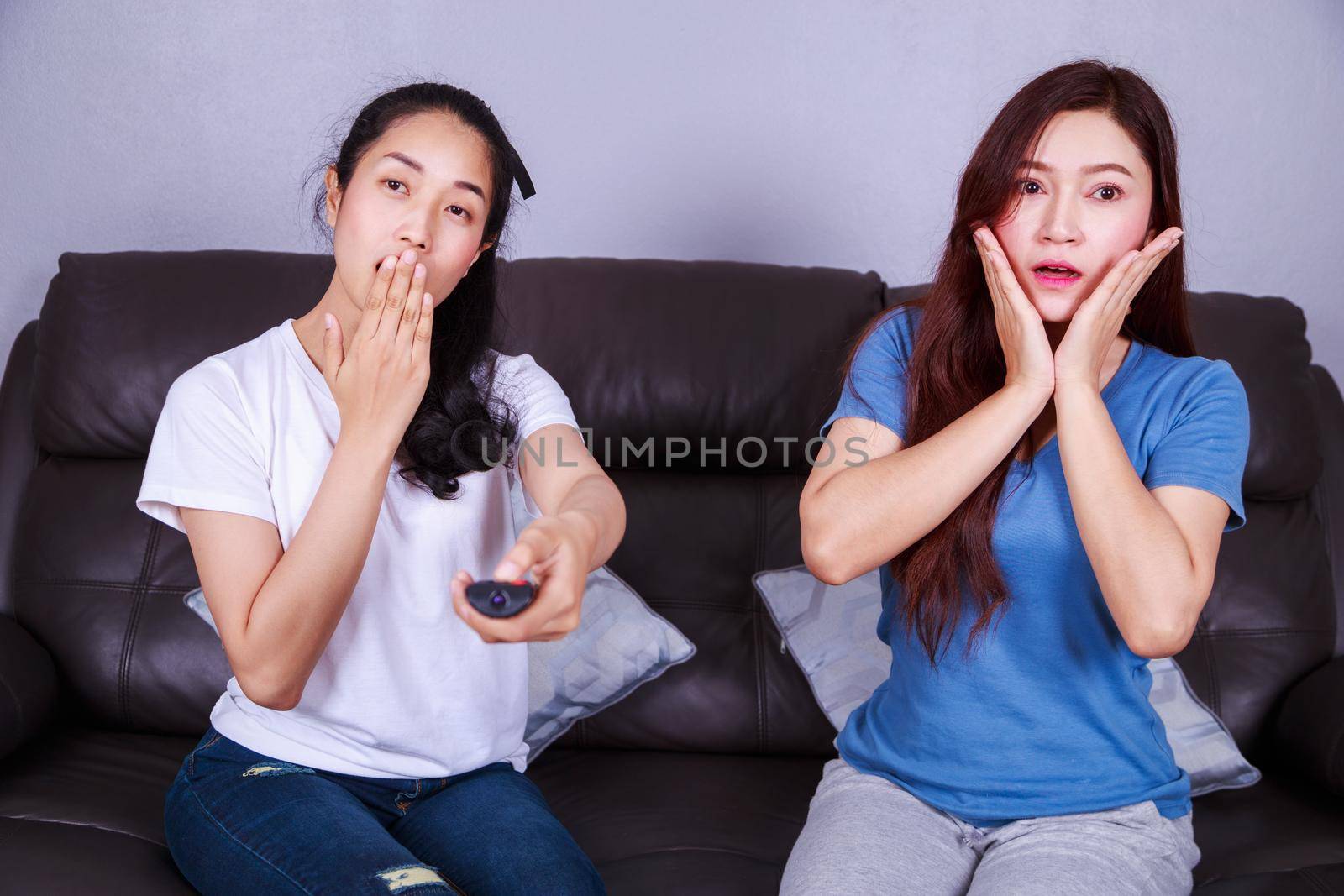 two scared woman sitting on sofa watching tv at home
