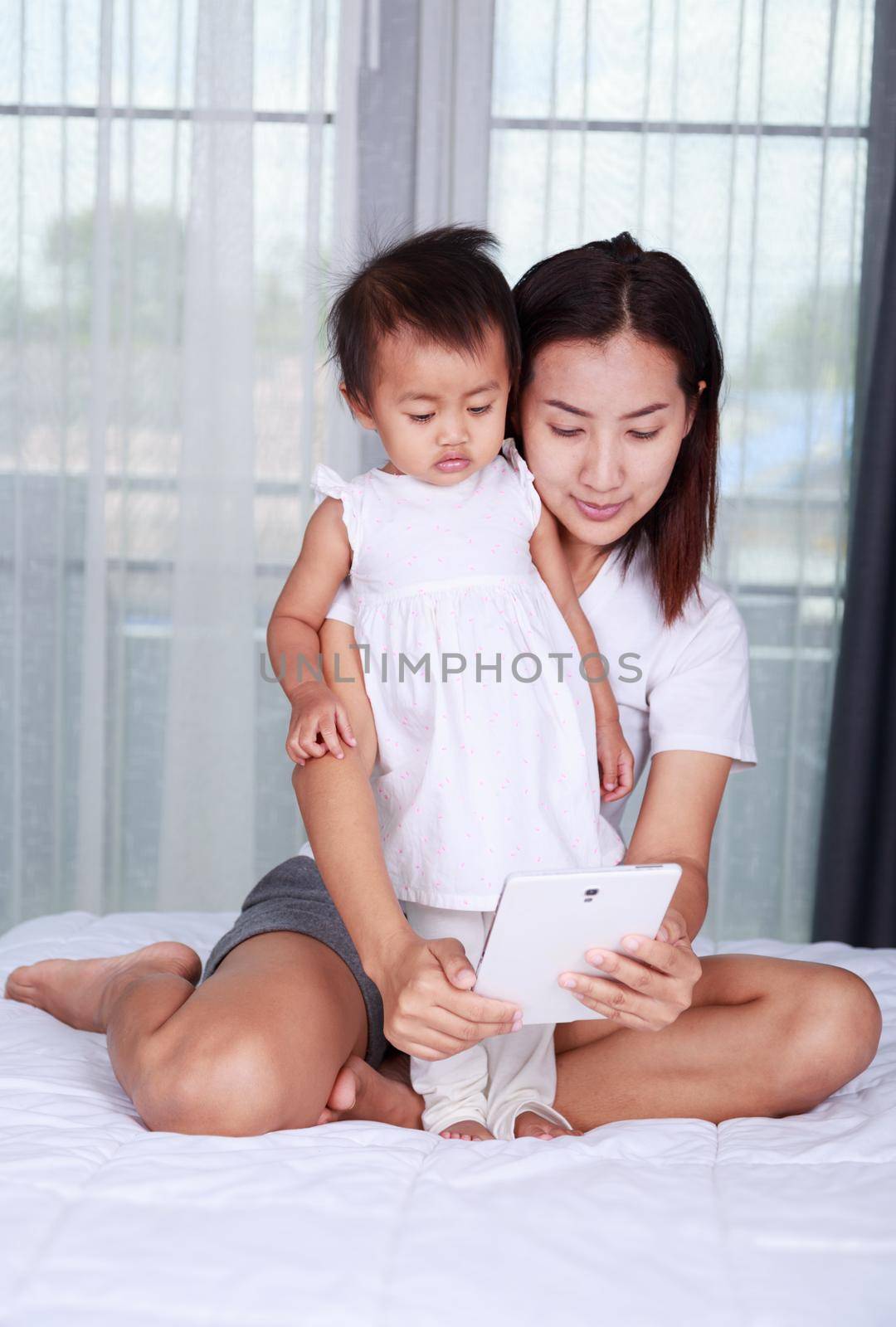 Mother and baby are looking to play and read tablet computer at home by geargodz