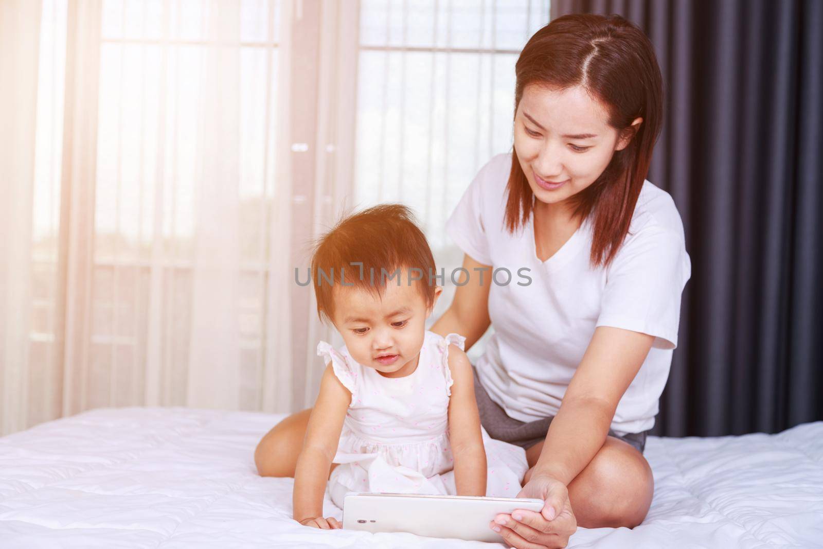 Mother and baby are looking to play and read tablet computer at home by geargodz