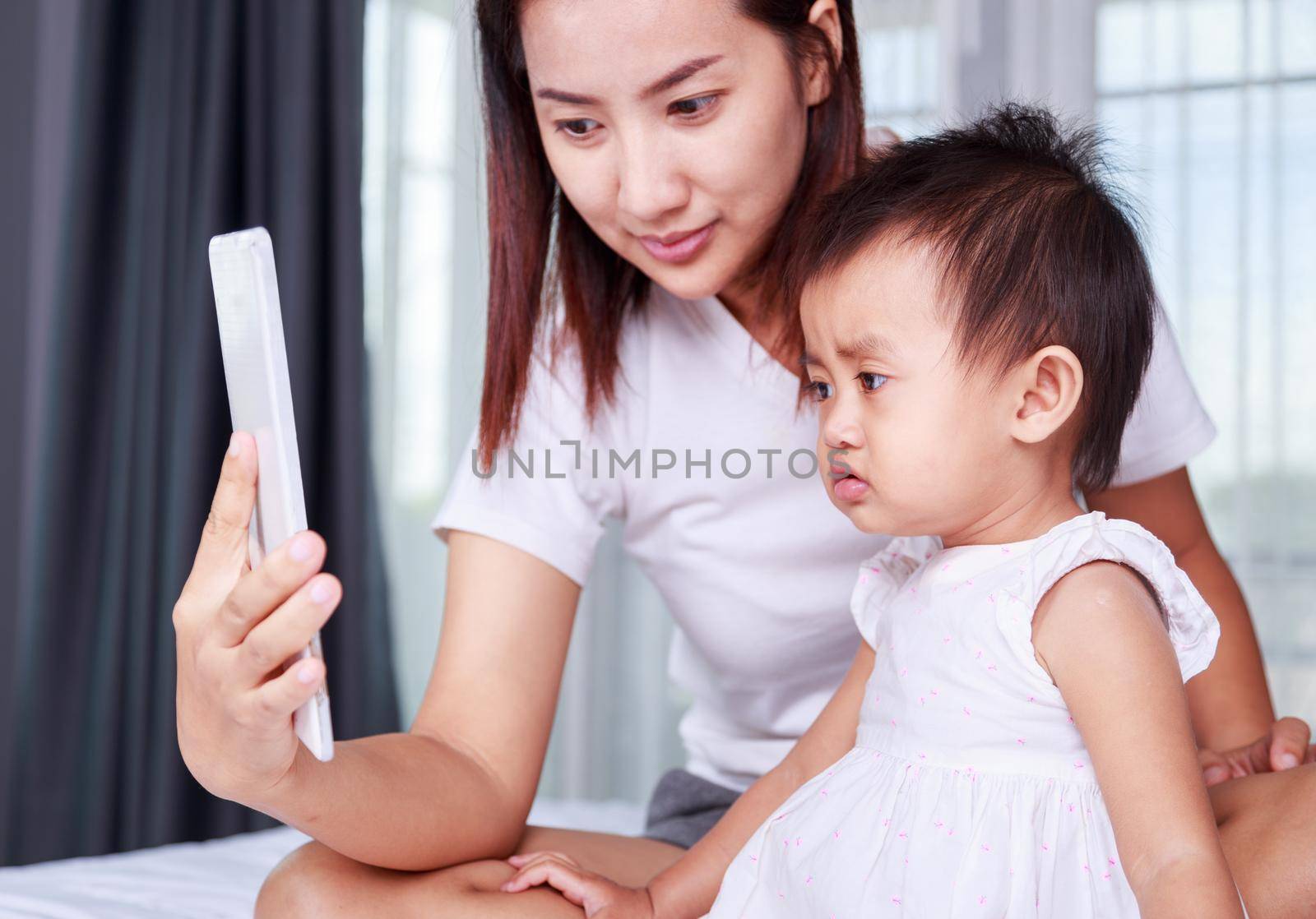 Mother and baby are looking to play and read tablet computer on bed at home