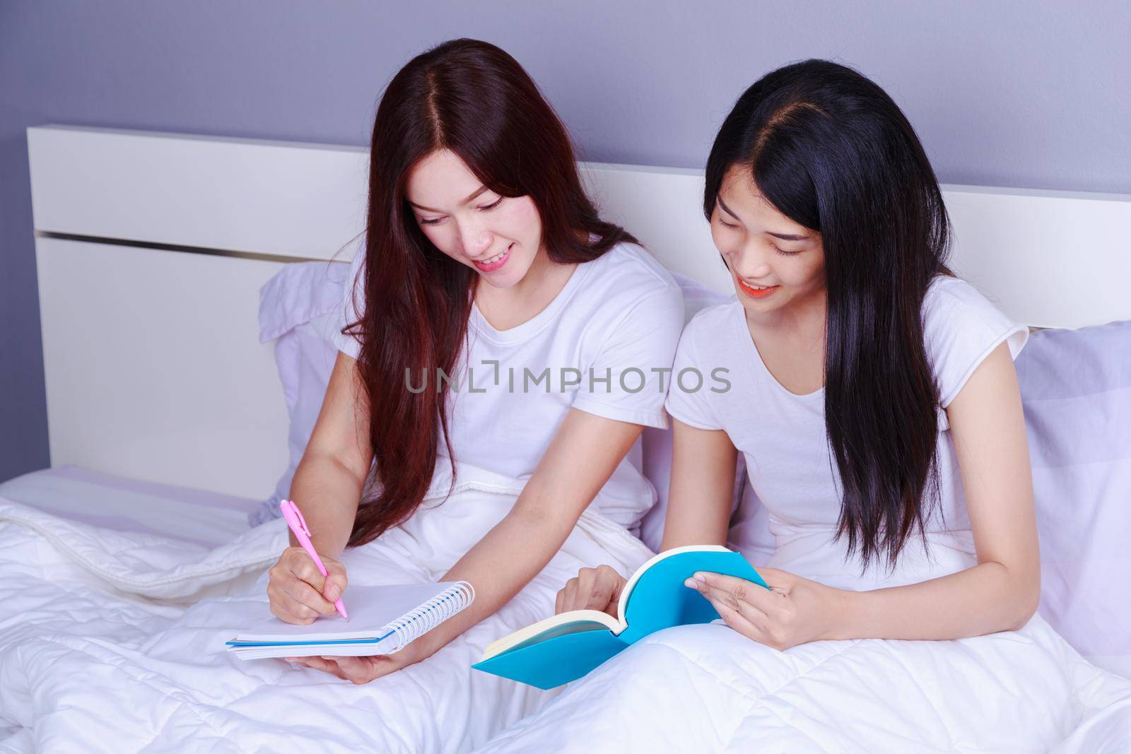 two woman writing and reading a book on bed in bedroom by geargodz