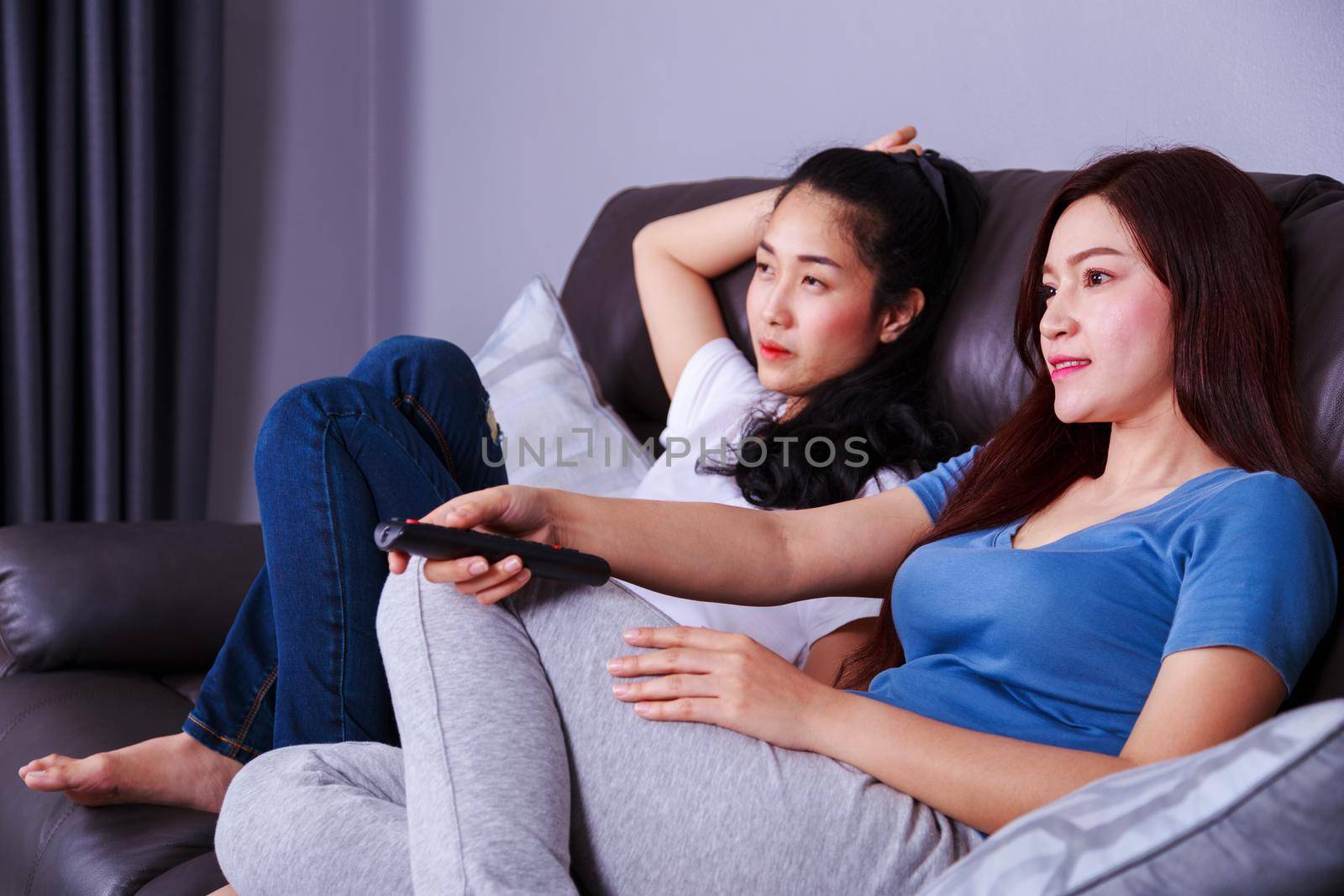 two best friends watching tv with remote on sofa in living room at home