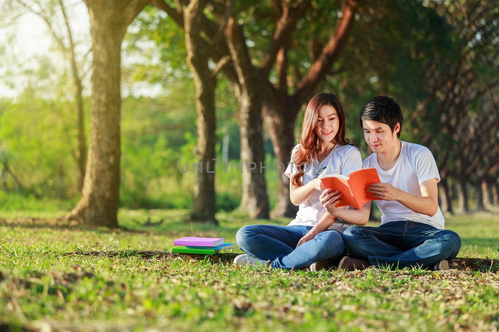 man and woman sitting and reading a book in the park