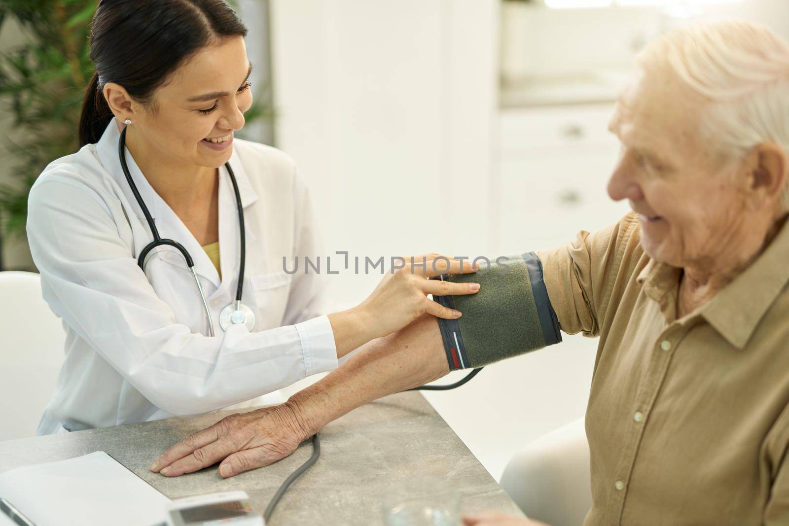 Amicable young doctor smiling while wrapping inflatable part of manometer around arm of an aged gentleman