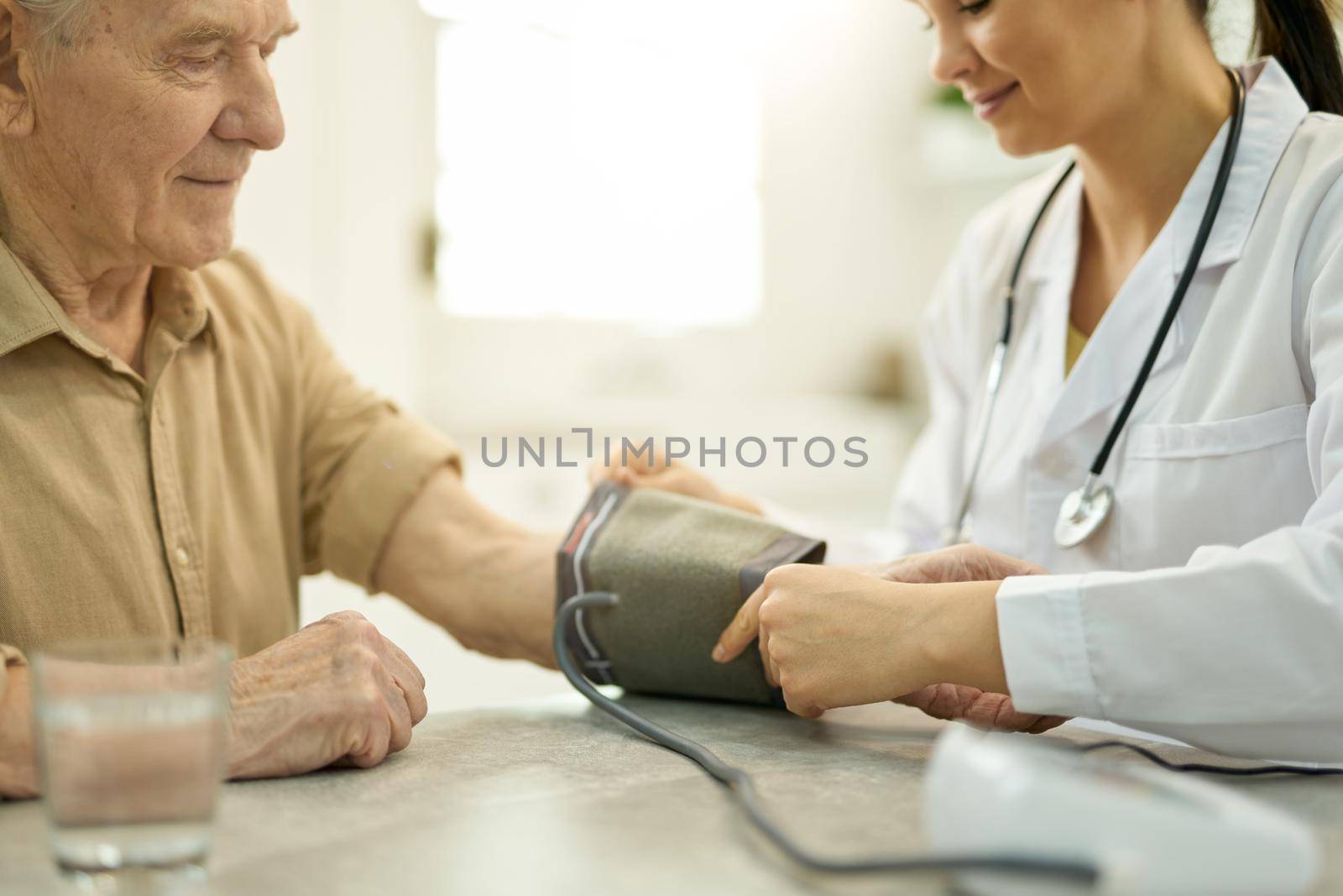 Caring medical doctor putting inflatable cuff of a manometer on arm of an aged man