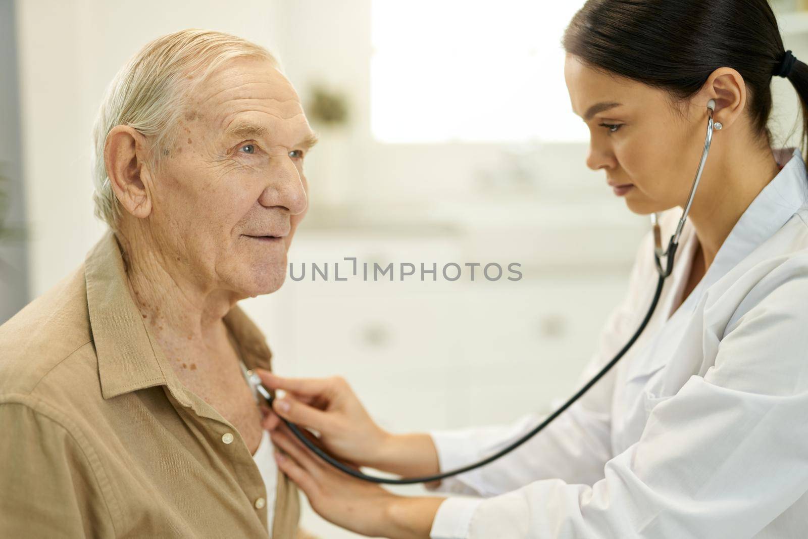 Qualified medic examining senior man lungs with stethoscope by friendsstock