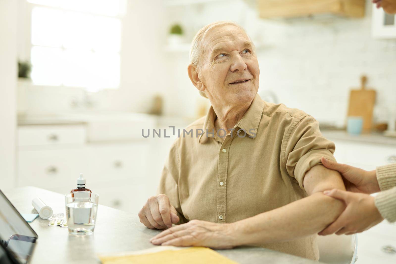 Senior citizen looking hoopeful while having his shoulder examined by medical worker at home