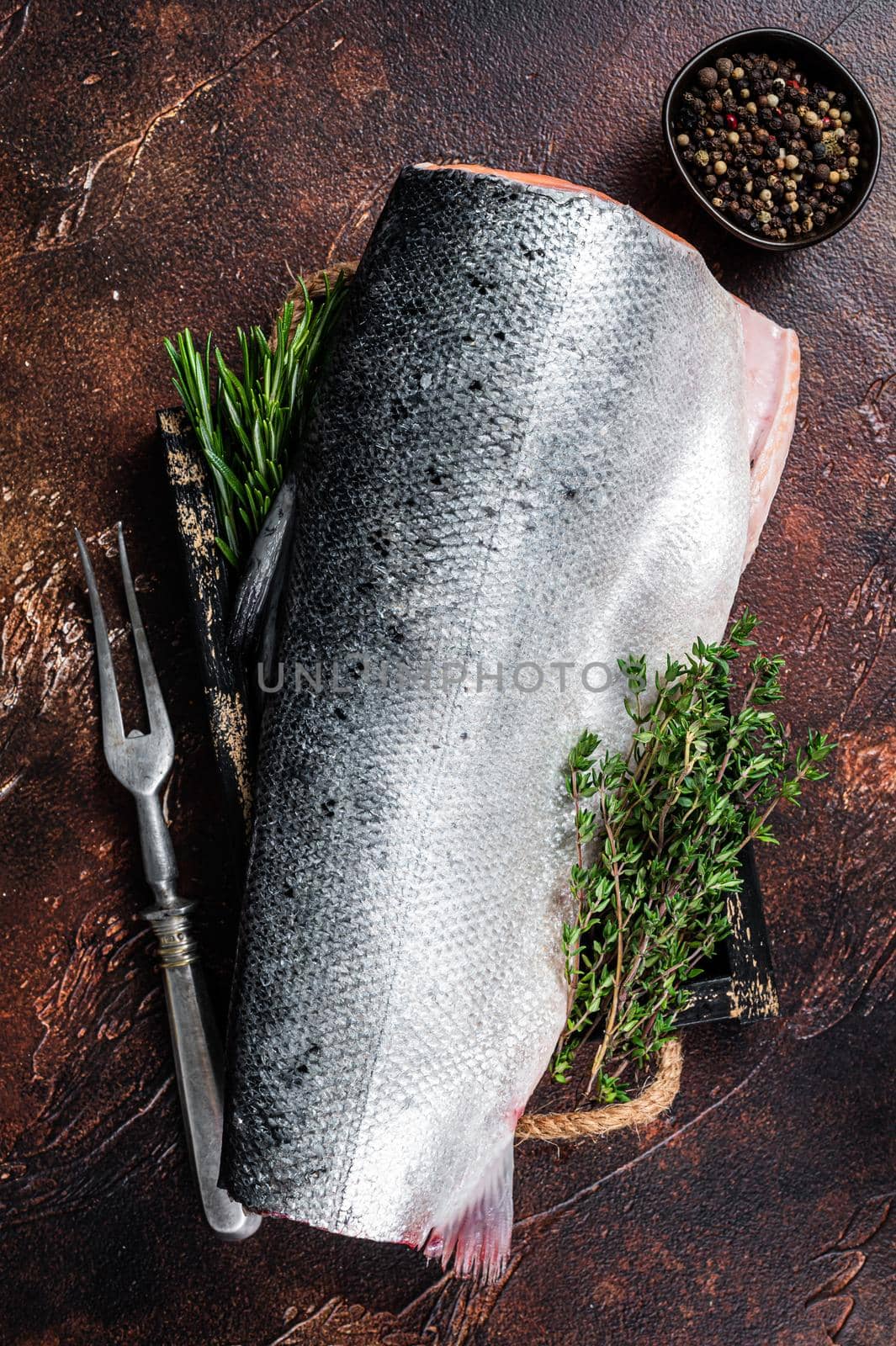 Slice of Raw cut salmon fish in a wooden tray with thyme. Dark background. Top view.