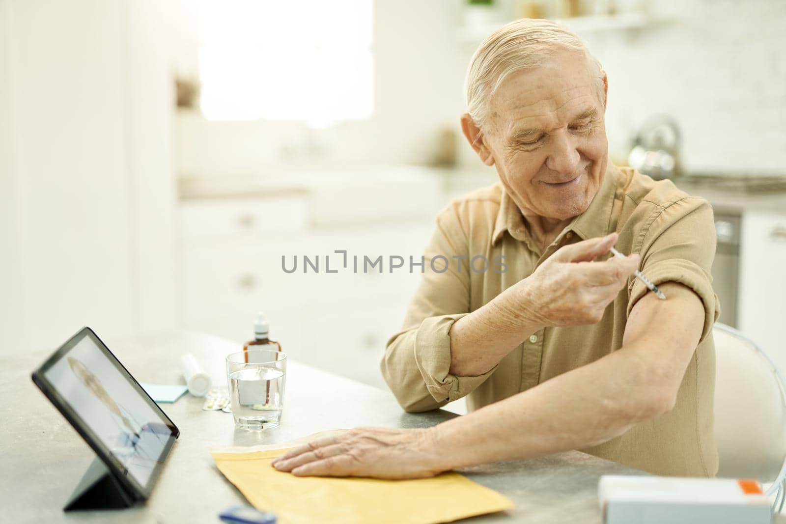 Gladsome aged man performing injection on his own arm by friendsstock