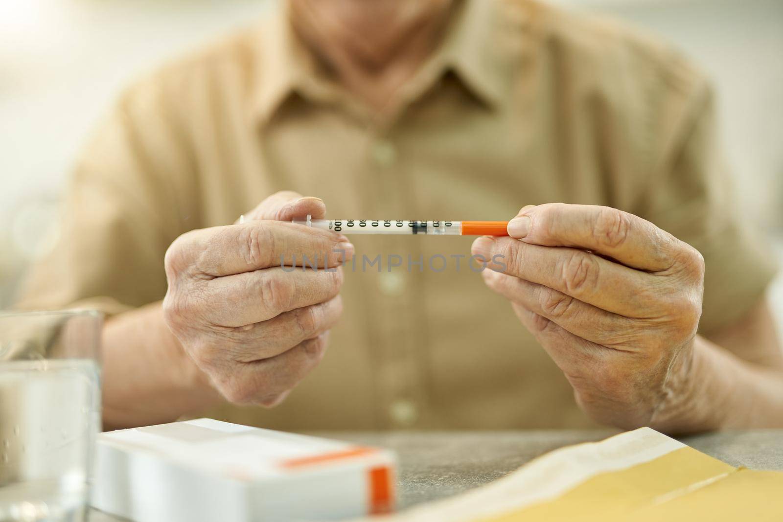 Cropped photo of eldelry person sitting at the table and holding a thin medical syringe