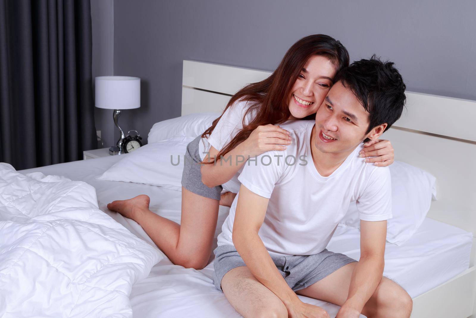 happy young attractive couple hugging on bed in bedroom by geargodz
