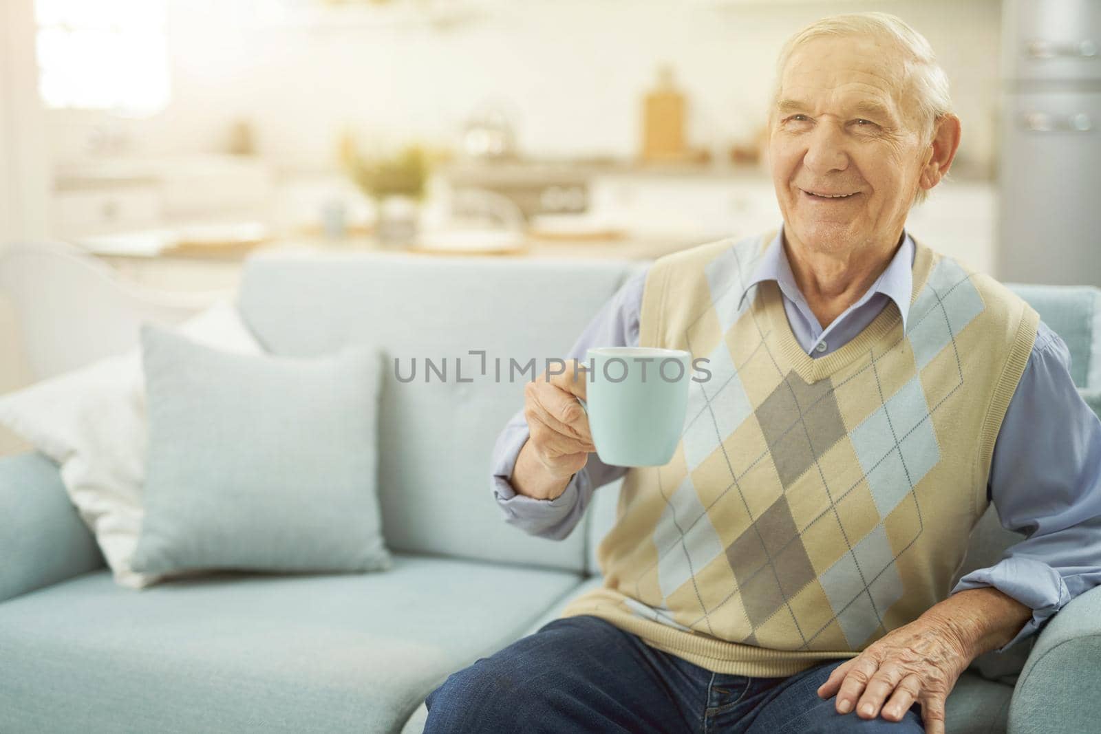 Happy old man resting on sofa with cup of tea by friendsstock