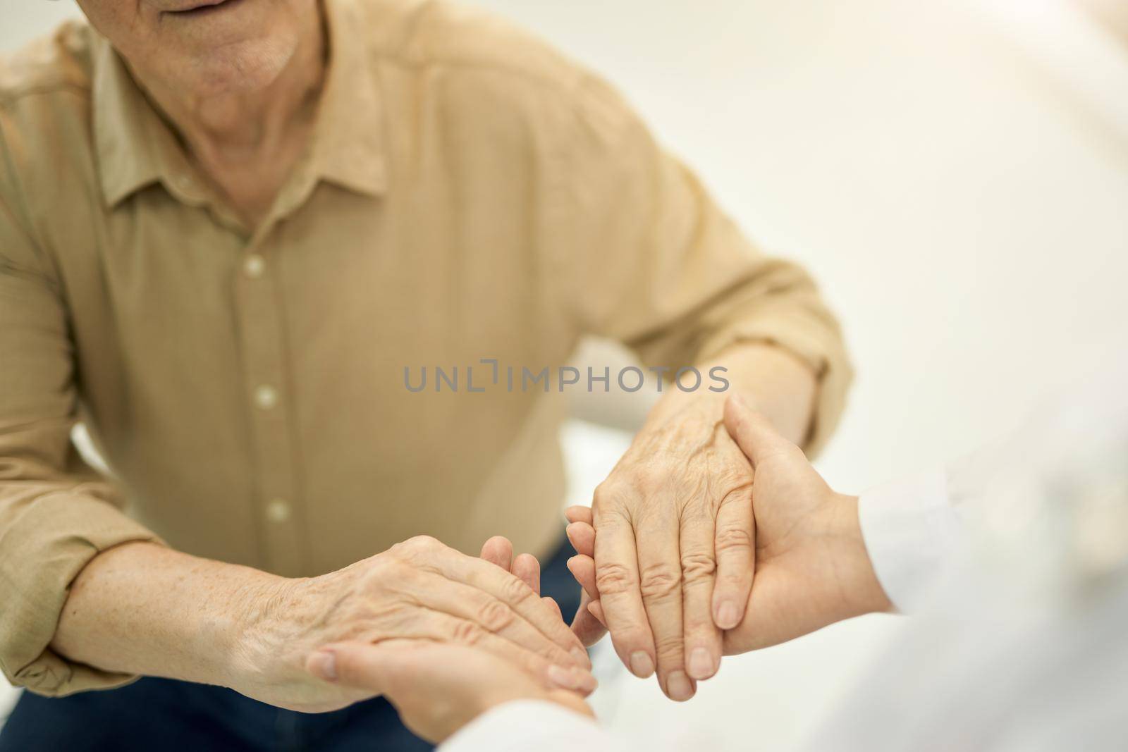 Cropped photo of medical worker holding hands of senior gentleman while examining his joints