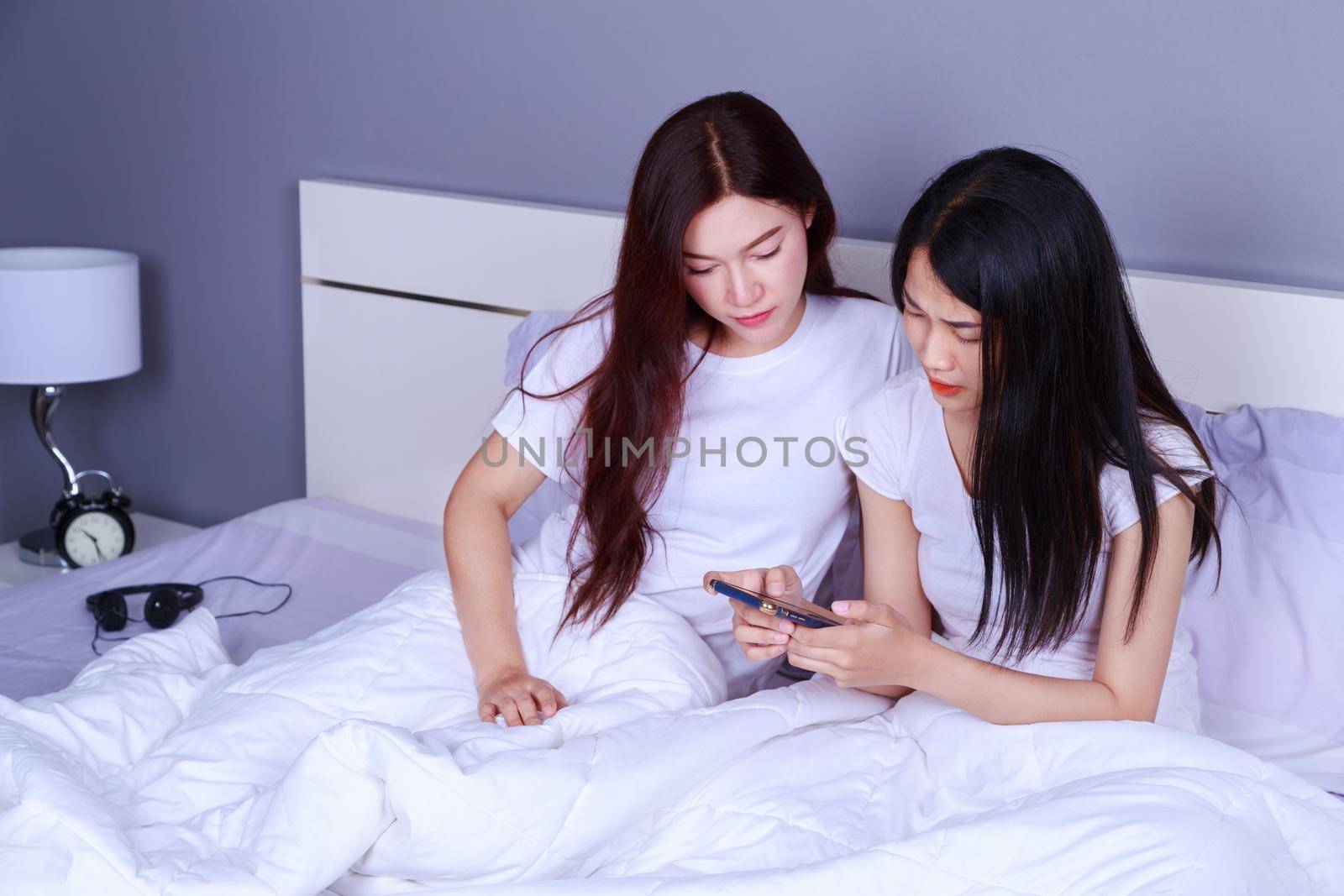 two woman using a phone in her hand on bed in the bedroom