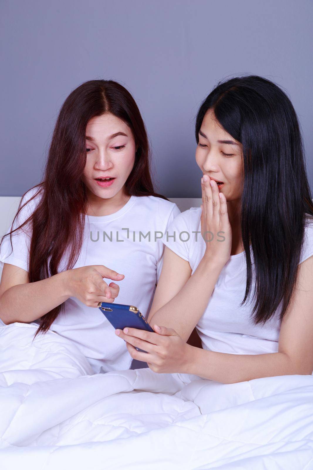 two shocked woman using a phone in her hand on bed in bedroom by geargodz