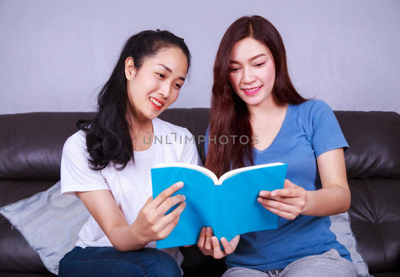 two young woman reading a book on sofa in living room at home