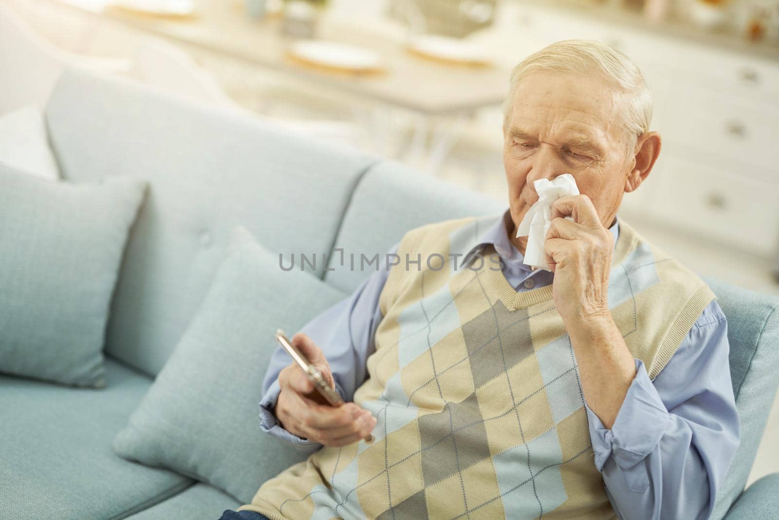Senior citizen using a paper napkin during an online consultation with a doctor while sitting on the couch