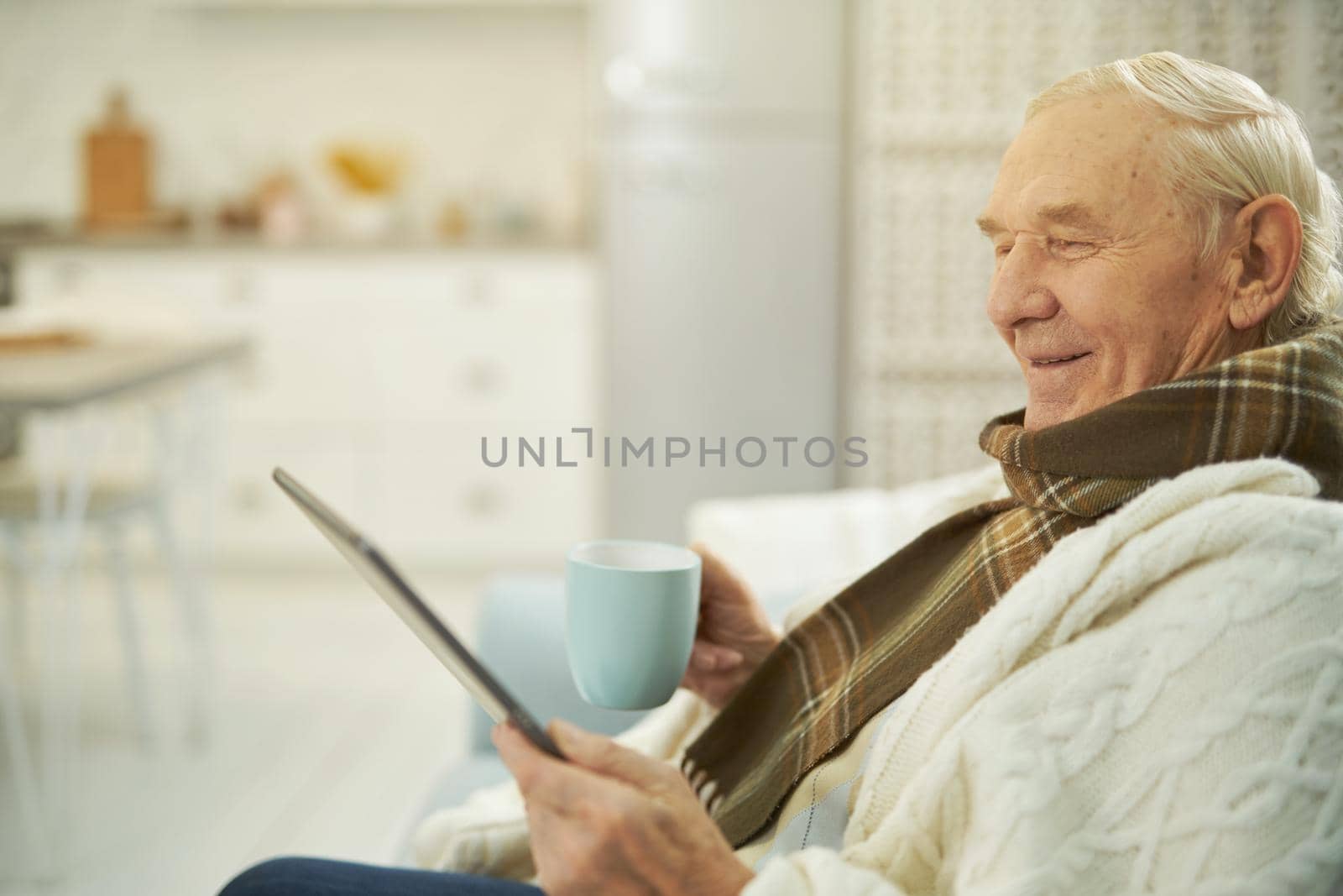 Happy man holding a cup of hot drink while looking at the tablet screen and making a video call with therapist