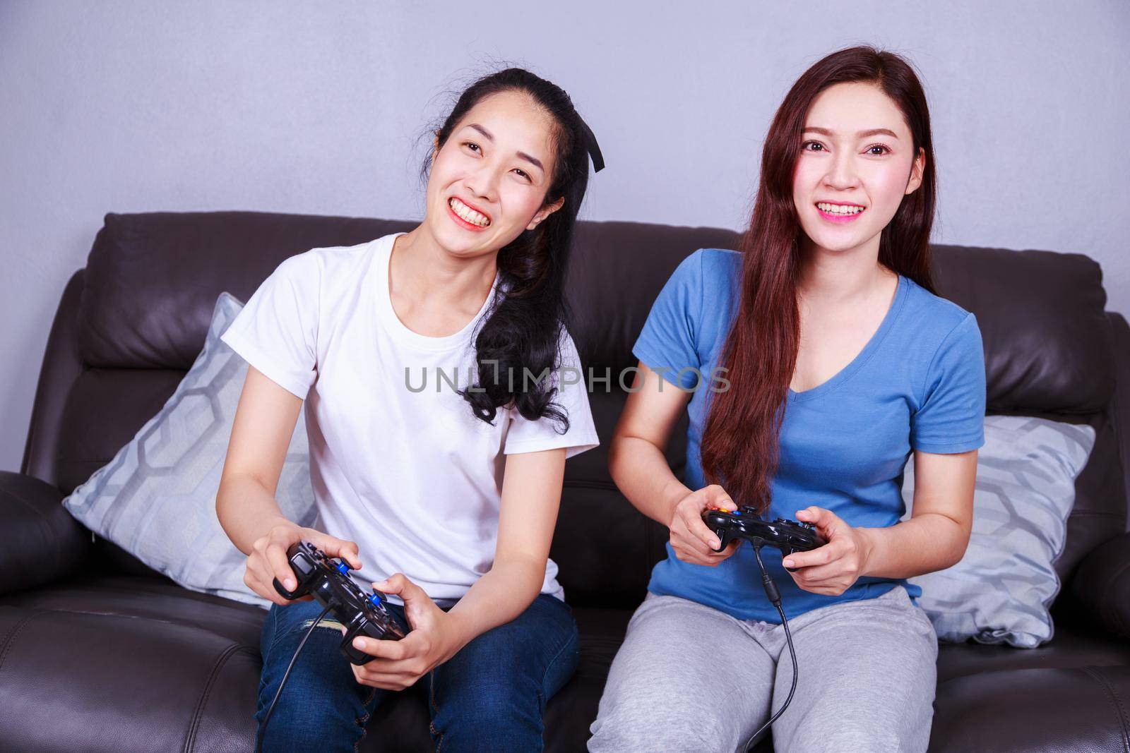 two young woman using joystick controller playing video game on sofa at home by geargodz