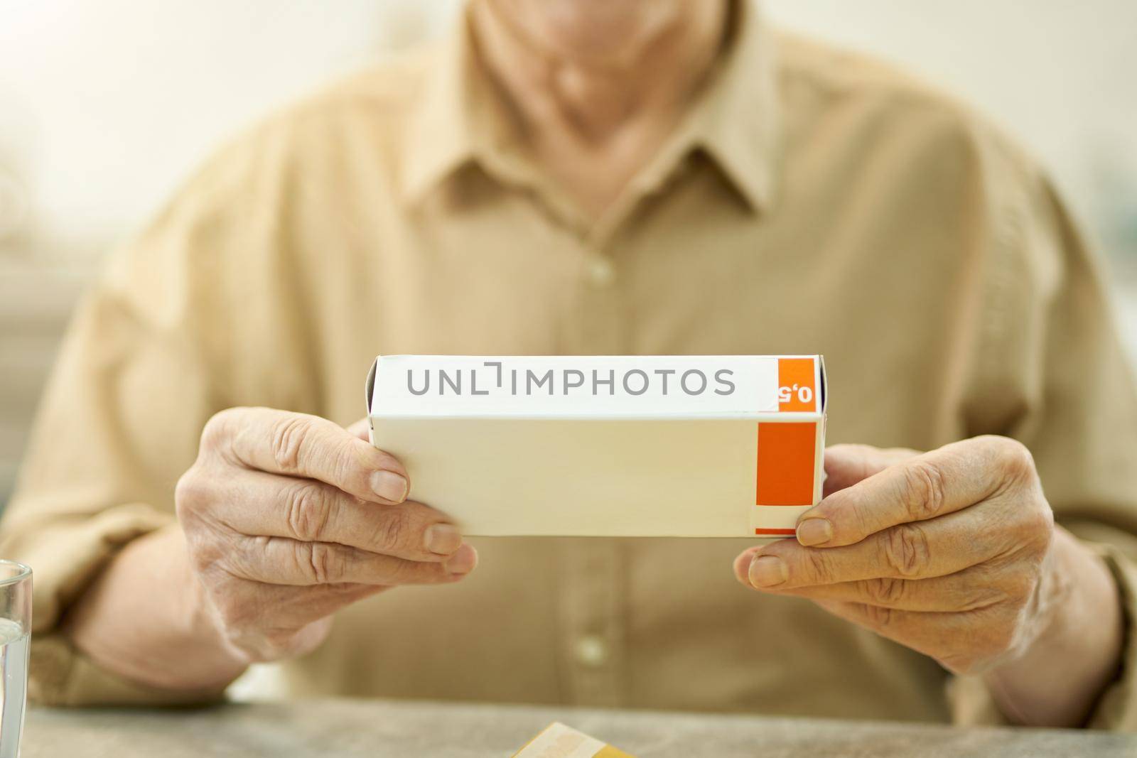 Copy space photo of senior man in button-up shirt holding a blank box of medication while sat at the table