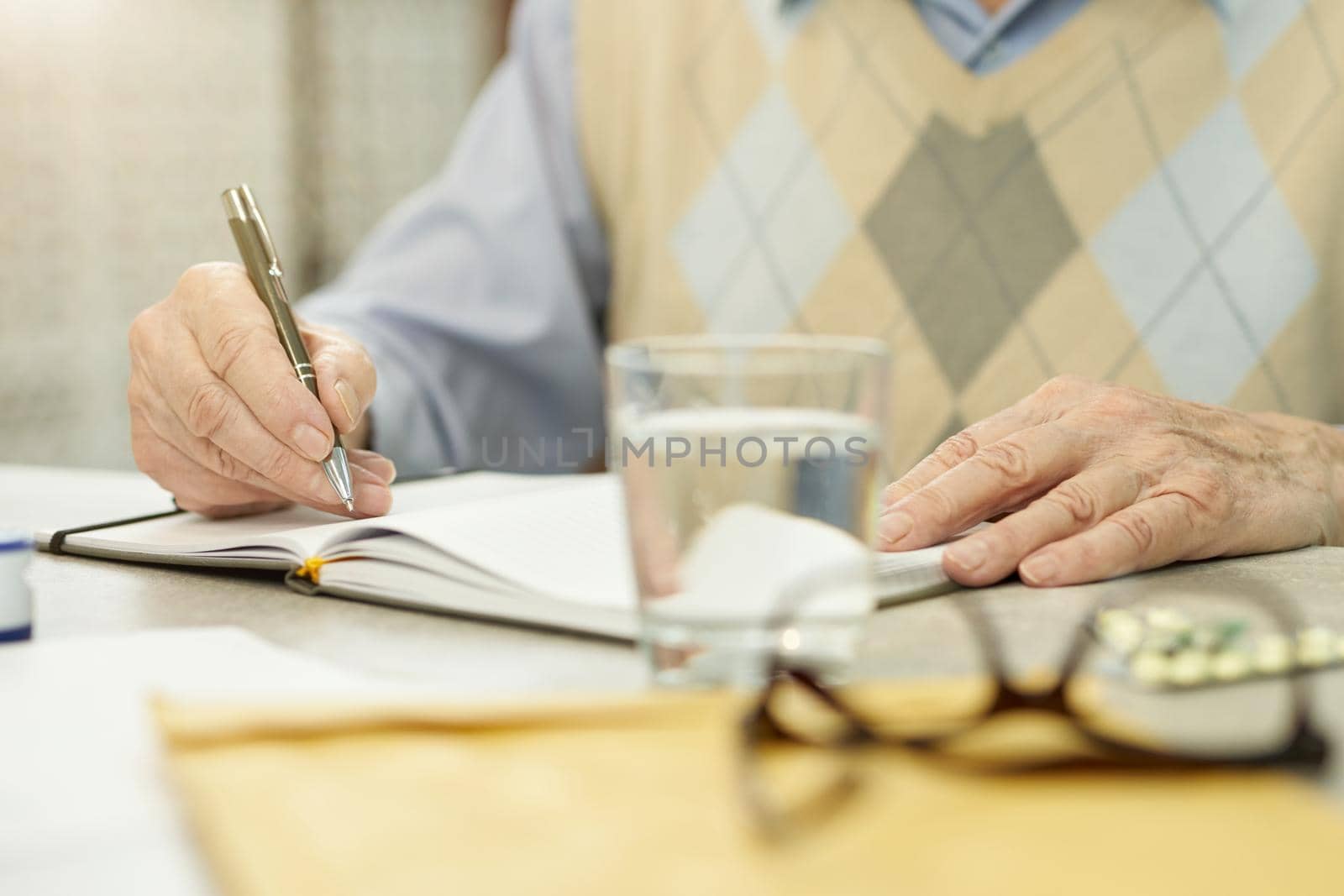 Cropped photo of an aged man writing in a notebook while sitting at the table