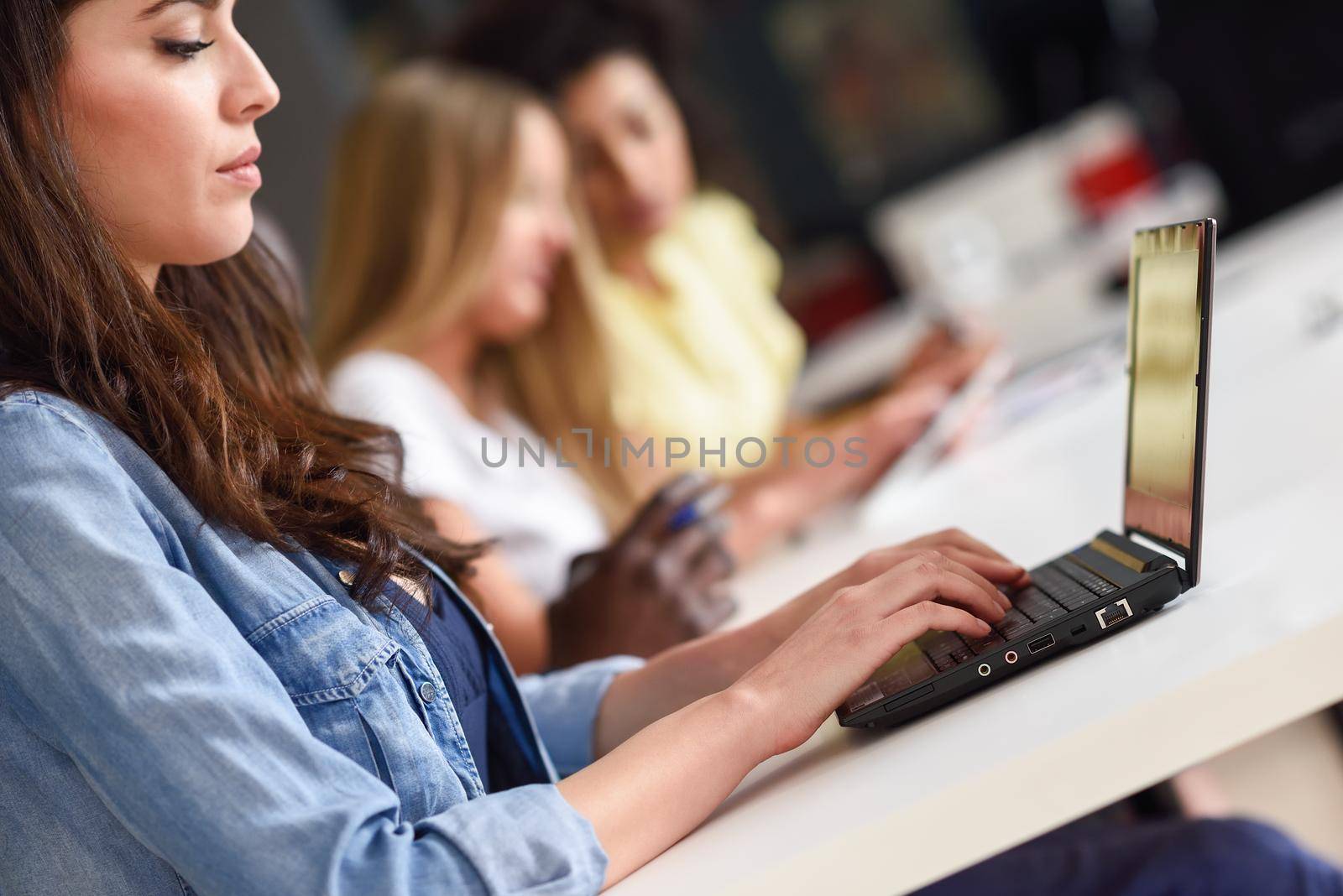 Young woman studying with laptop computer on white desk. Beautiful girls and guys working together wearing casual clothes. Multi-ethnic coworkers group.