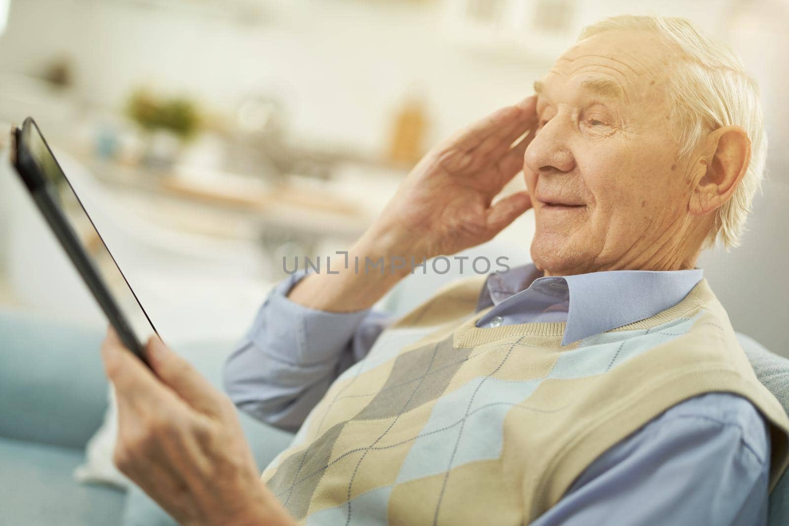 Pensioner holding gadget while looking at the tablet screen and making a video call with doctor