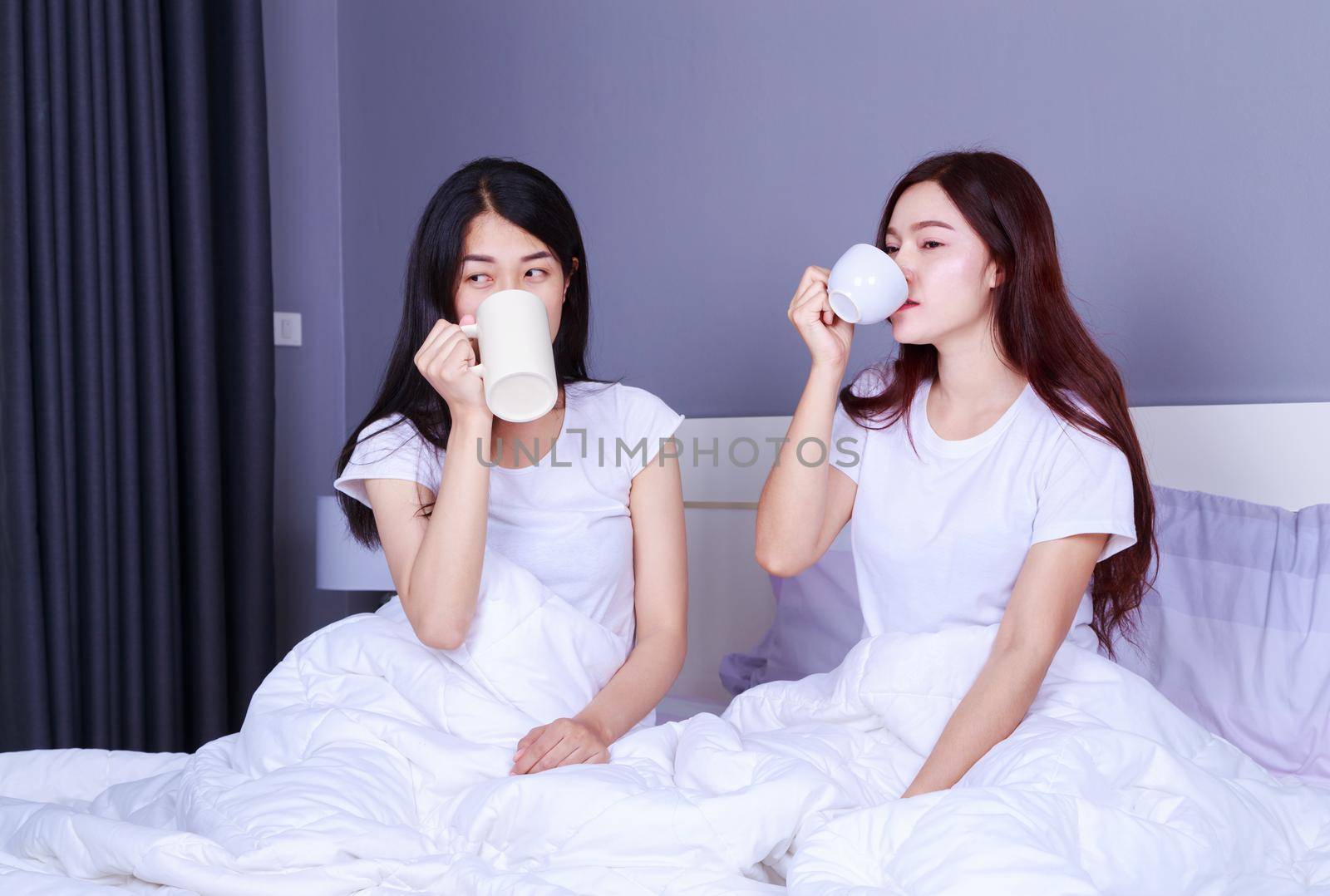 two best friends talking and drinking a cup of coffee on bed in the bedroom 