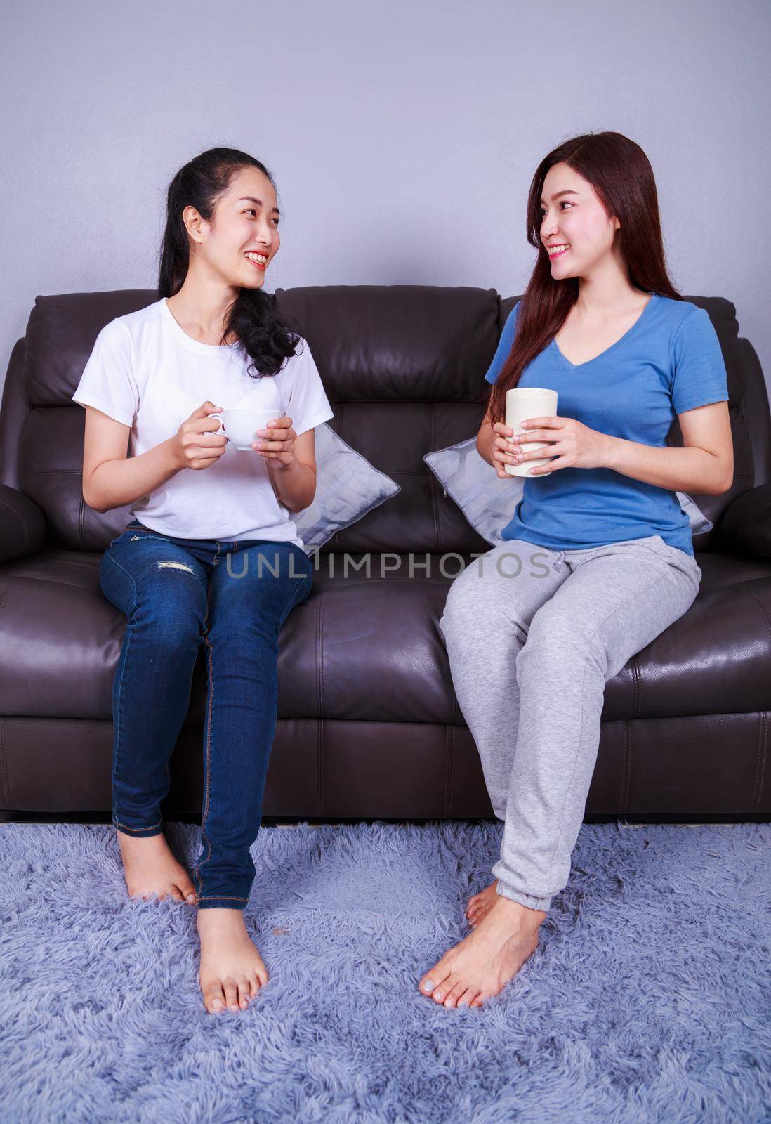 two best friends talking and drinking a cup of coffee on sofa in living room at home