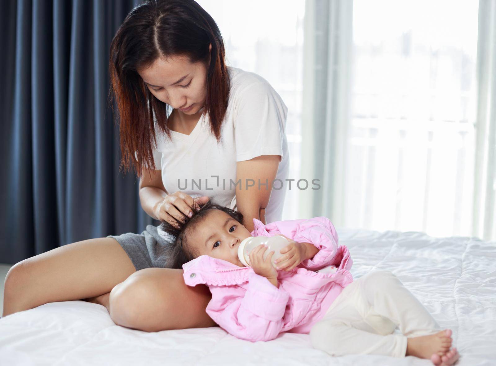 baby drinking a milk from bottle with mother on a bed