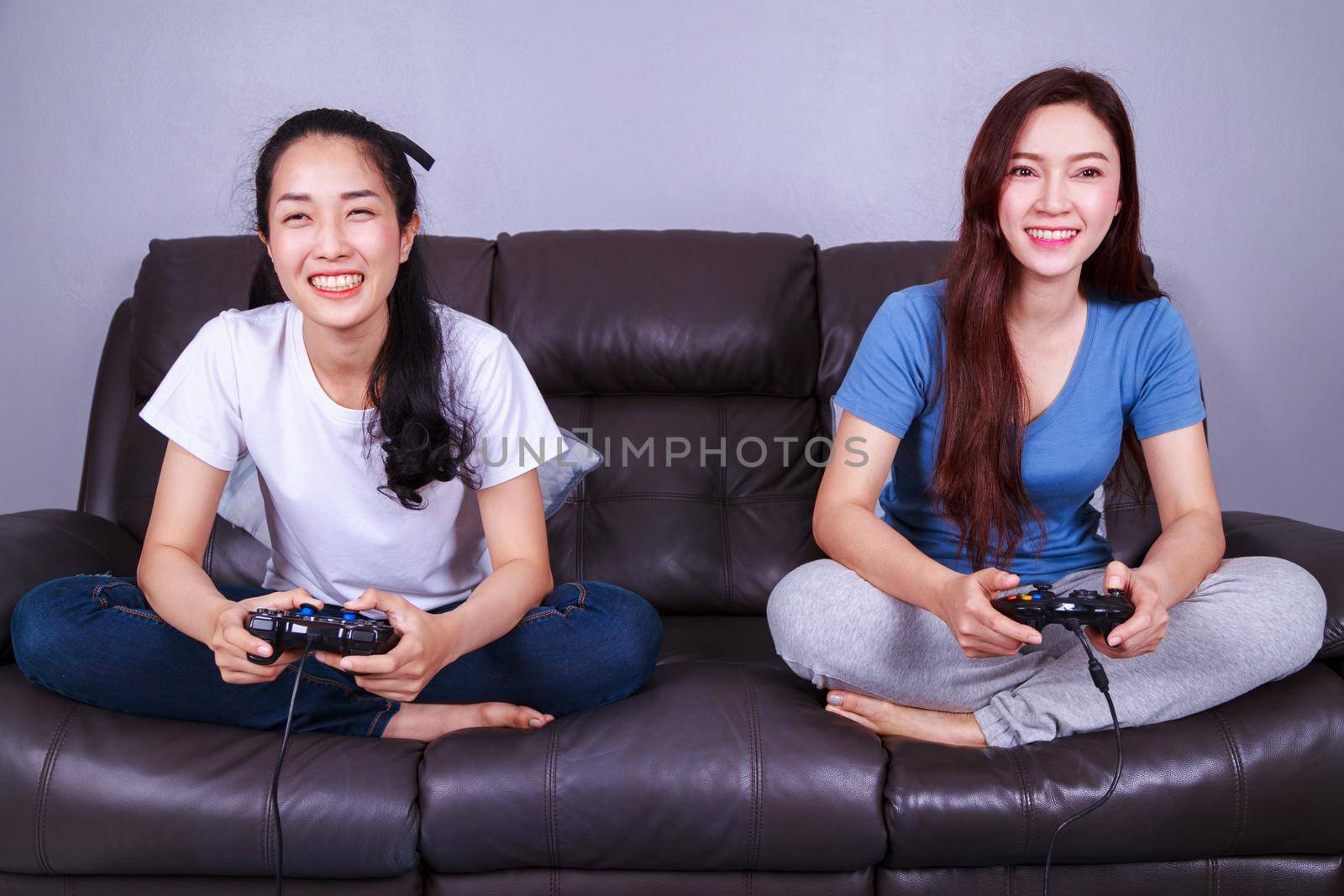 two young woman using joystick controller playing video game on sofa at home by geargodz