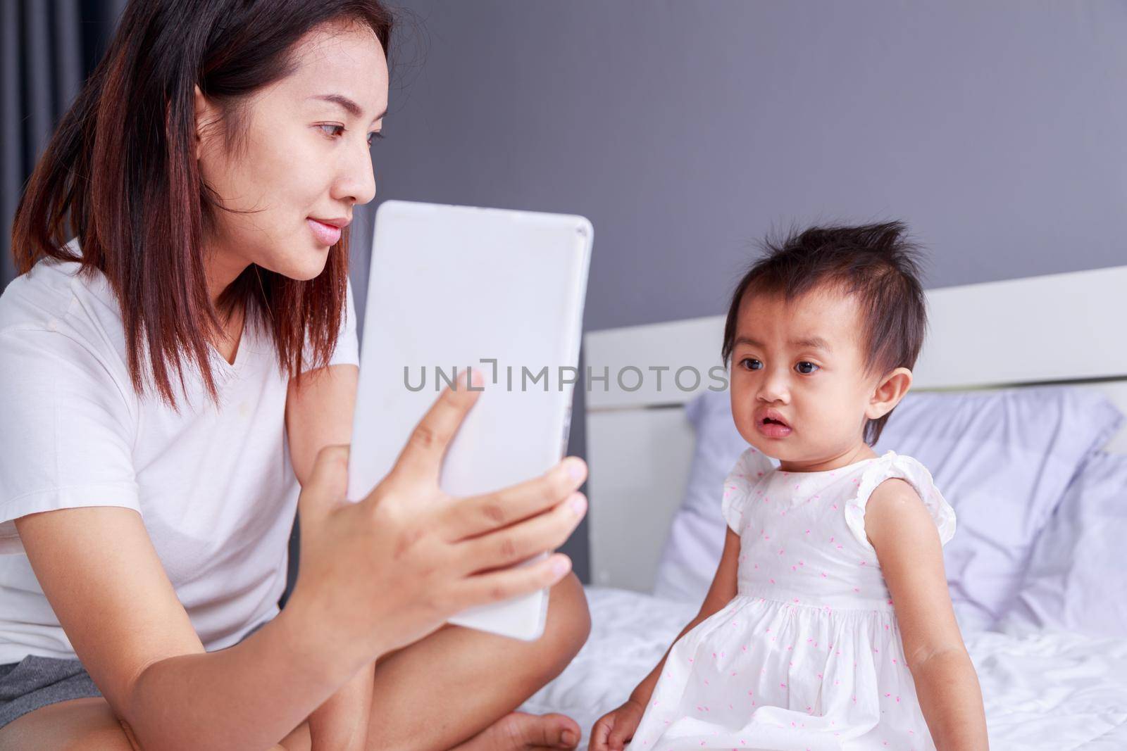 Mother and baby are looking to play and read tablet computer on bed at home