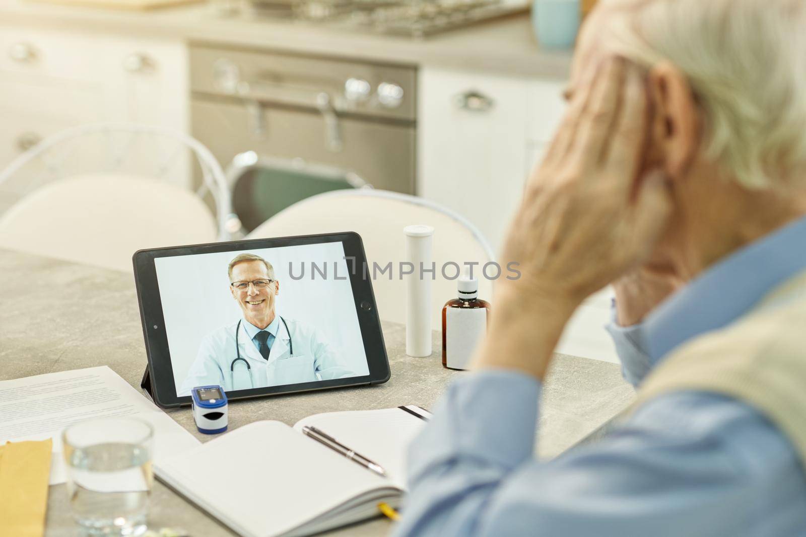 Cropped photo of smiley healthcare professional appearing on tablet screen while having online consultation with eldelry patient