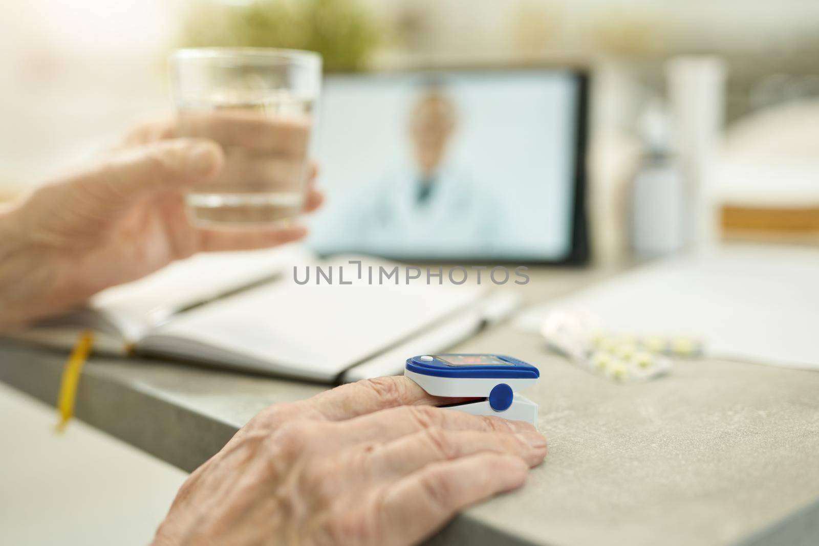 Selective focus photo of senior citizen using a tiny fingertip medical device and holding glass of water