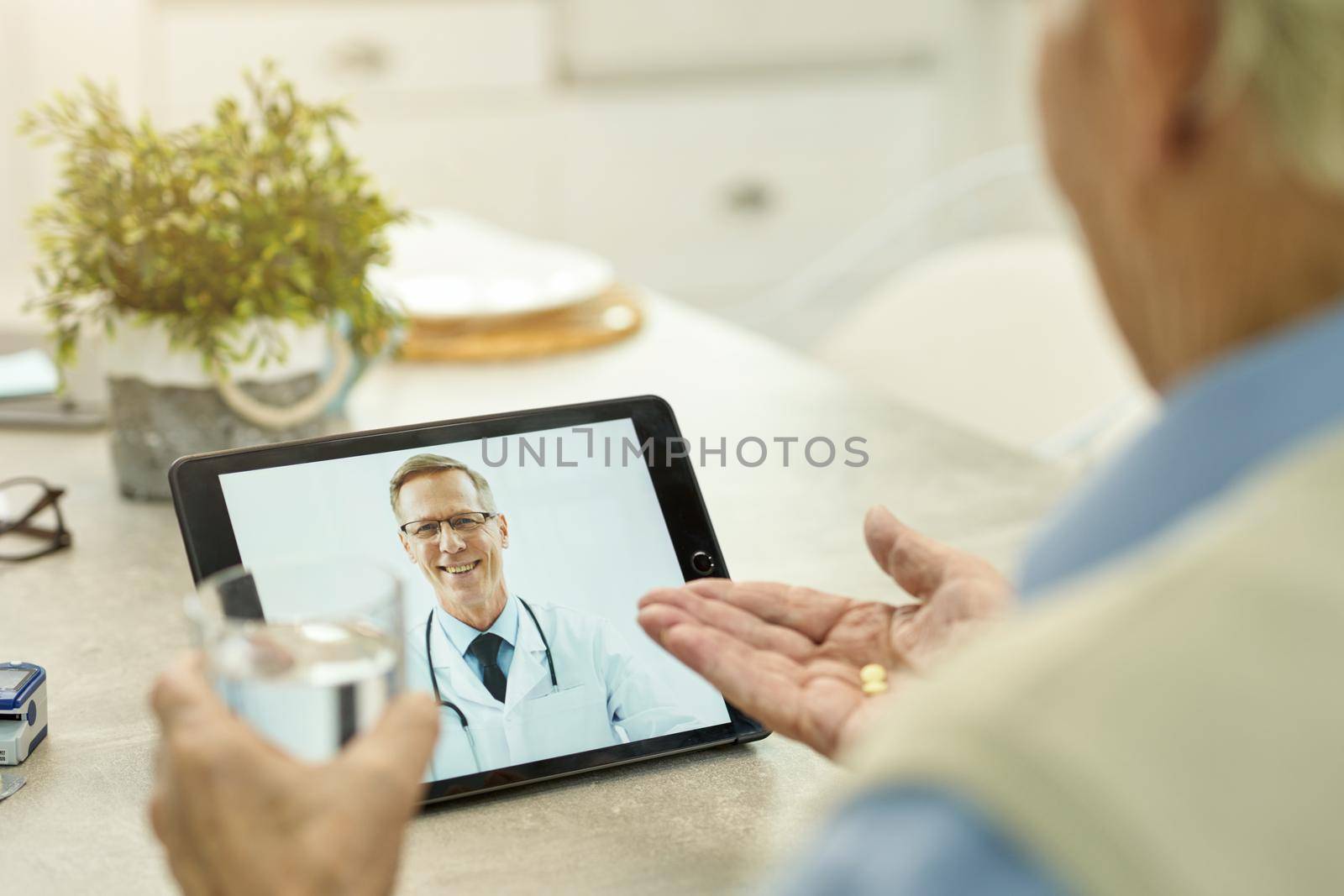 Professional medical doctor video-calling his senior patient and watching him take his medication with water