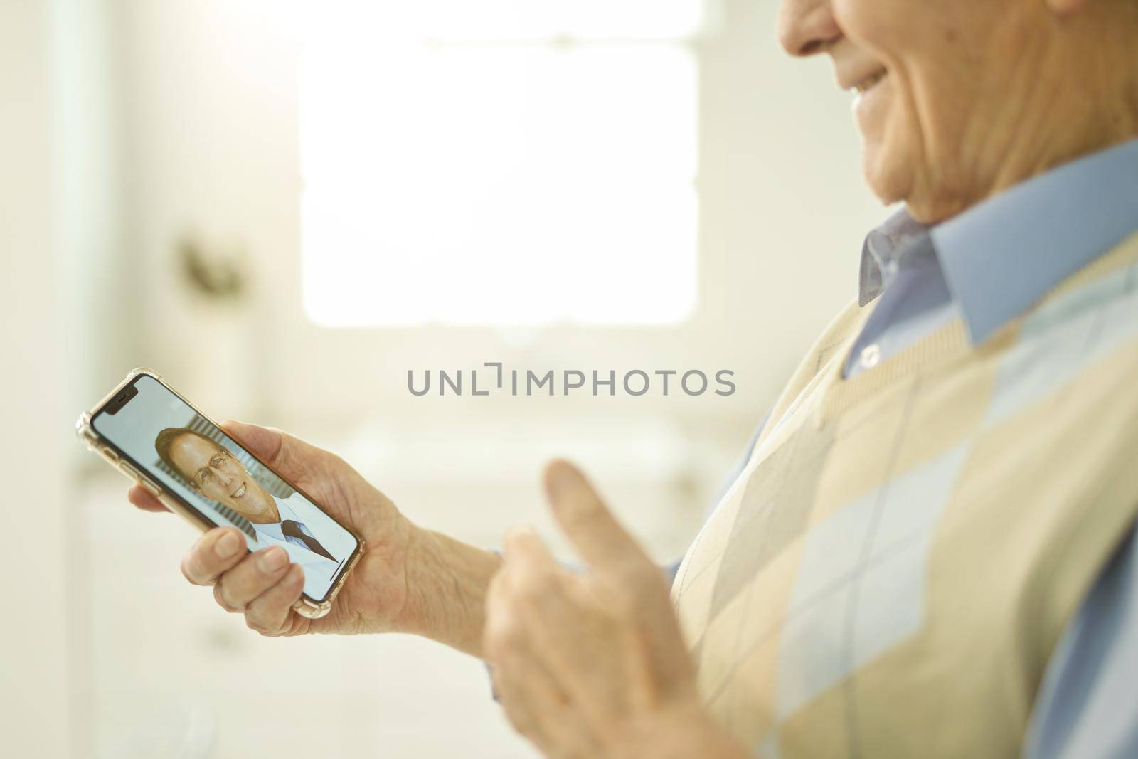 Cropped photo of a senior gentleman showing thumbs up to his doctor while consulting him on video-call